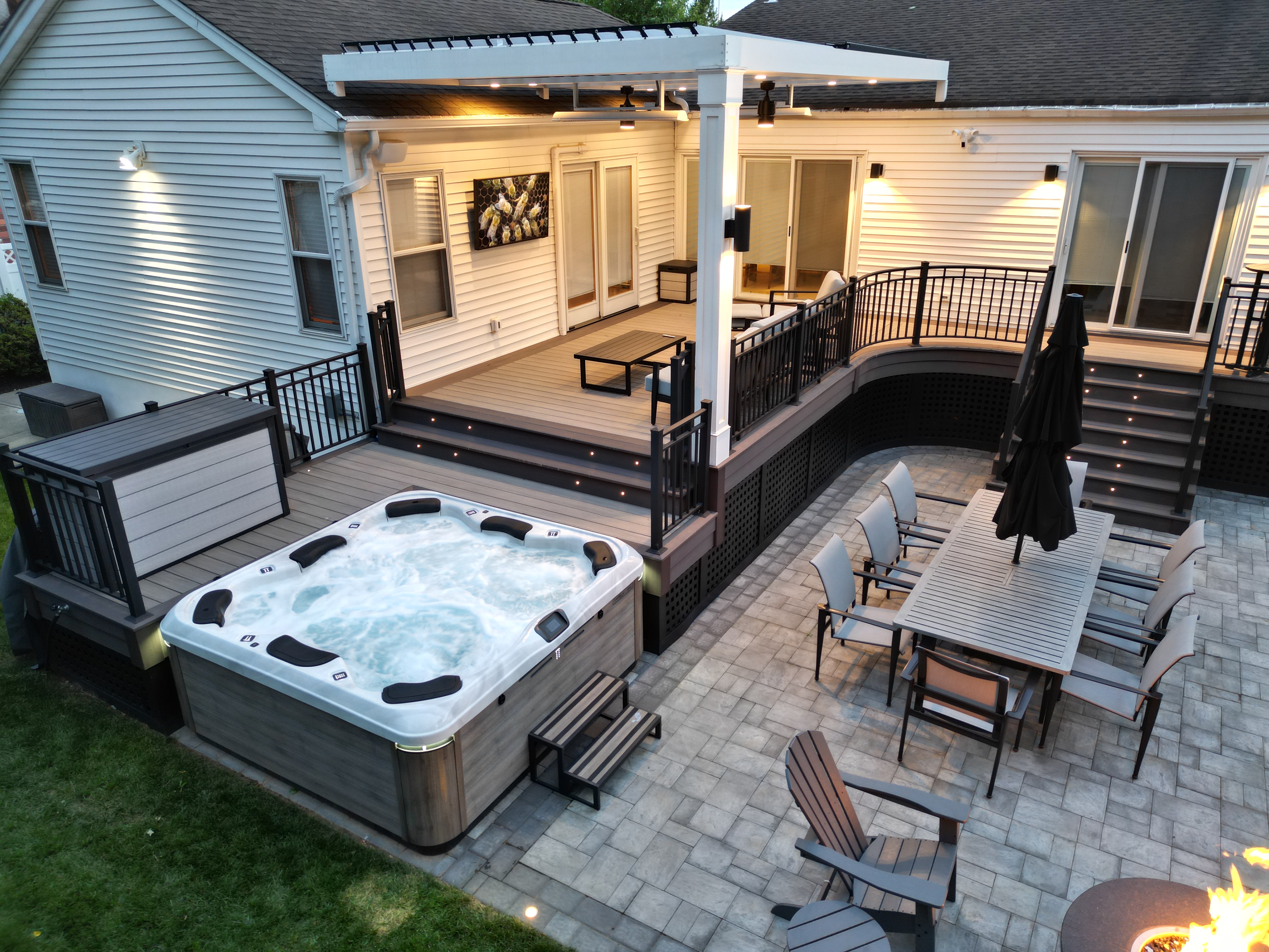space-efficient backyard design with multi-level PVC deck, built-in hot tub, step lighting, outdoor dining area, and compact paver patio layout