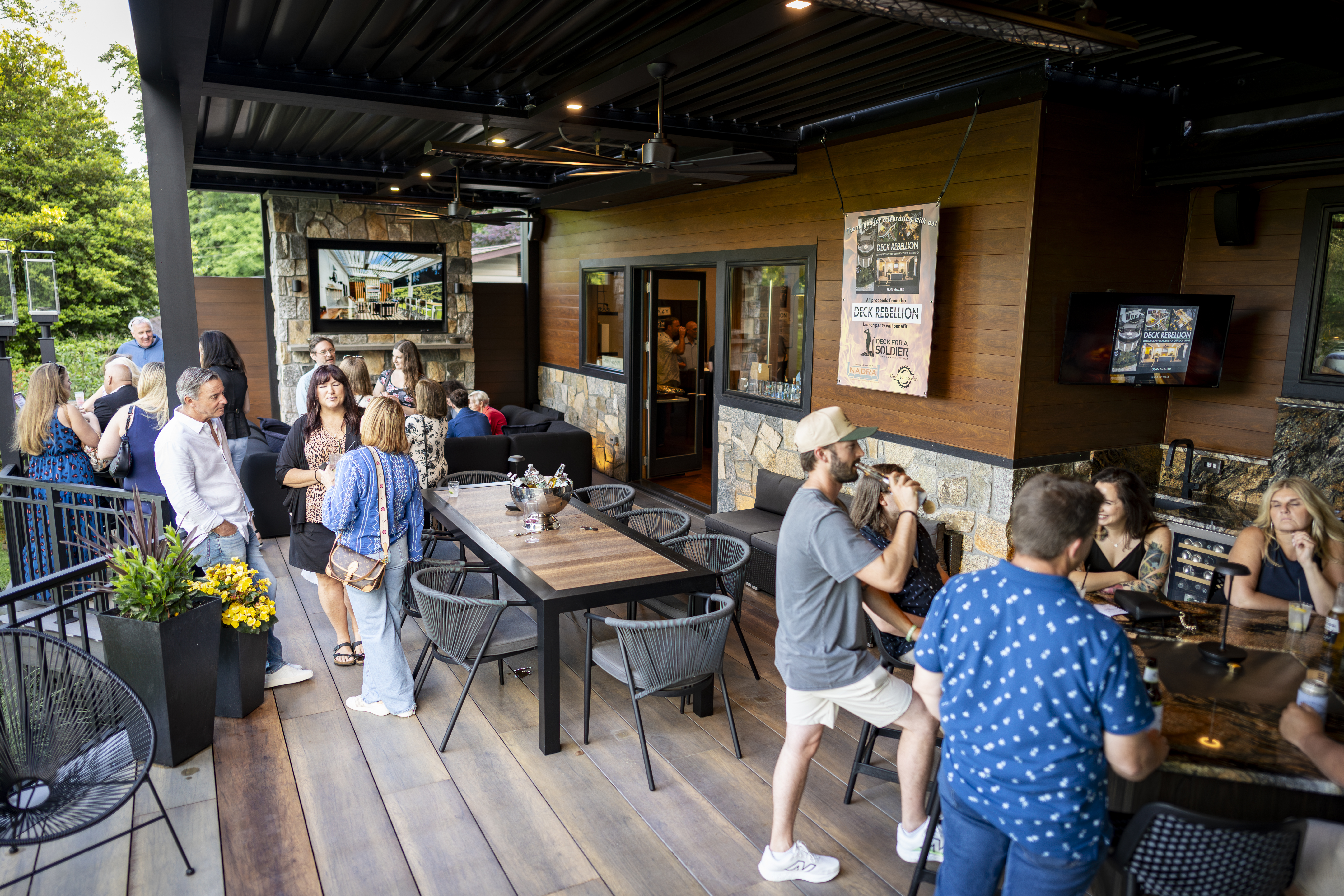 group of guests gathered on a covered backyard deck enjoying drinks and conversation at an outdoor bar and dining area