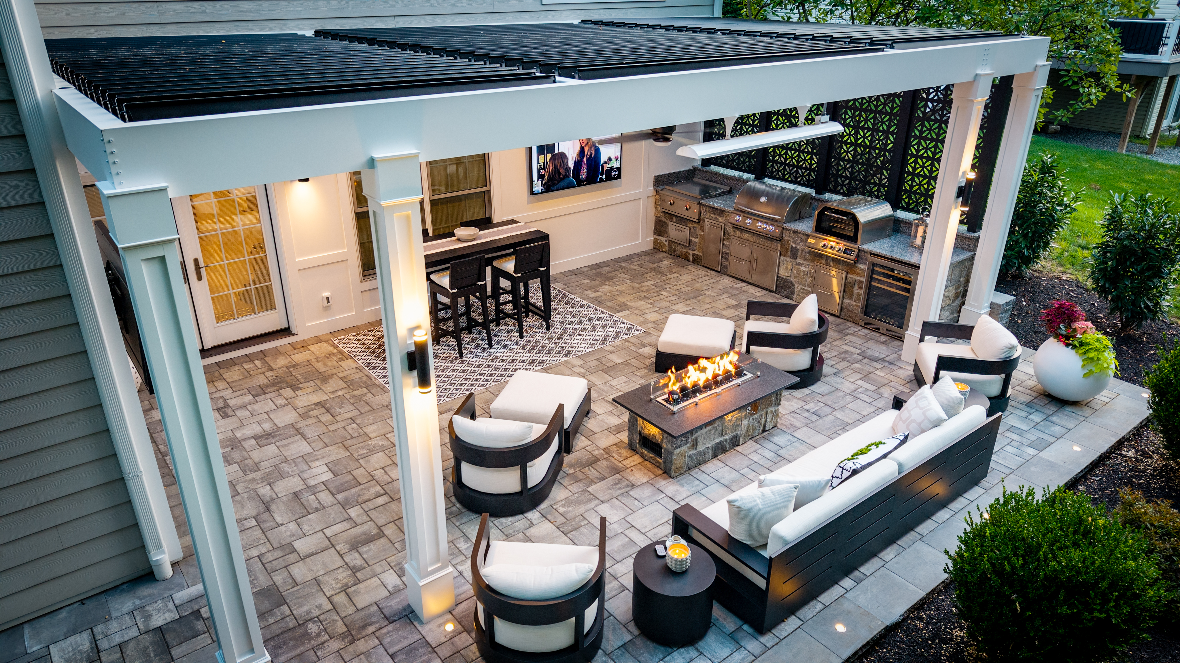 paver patio with black louvered roof, outdoor kitchen, lounge seating, linear fire table, and decorative privacy screen