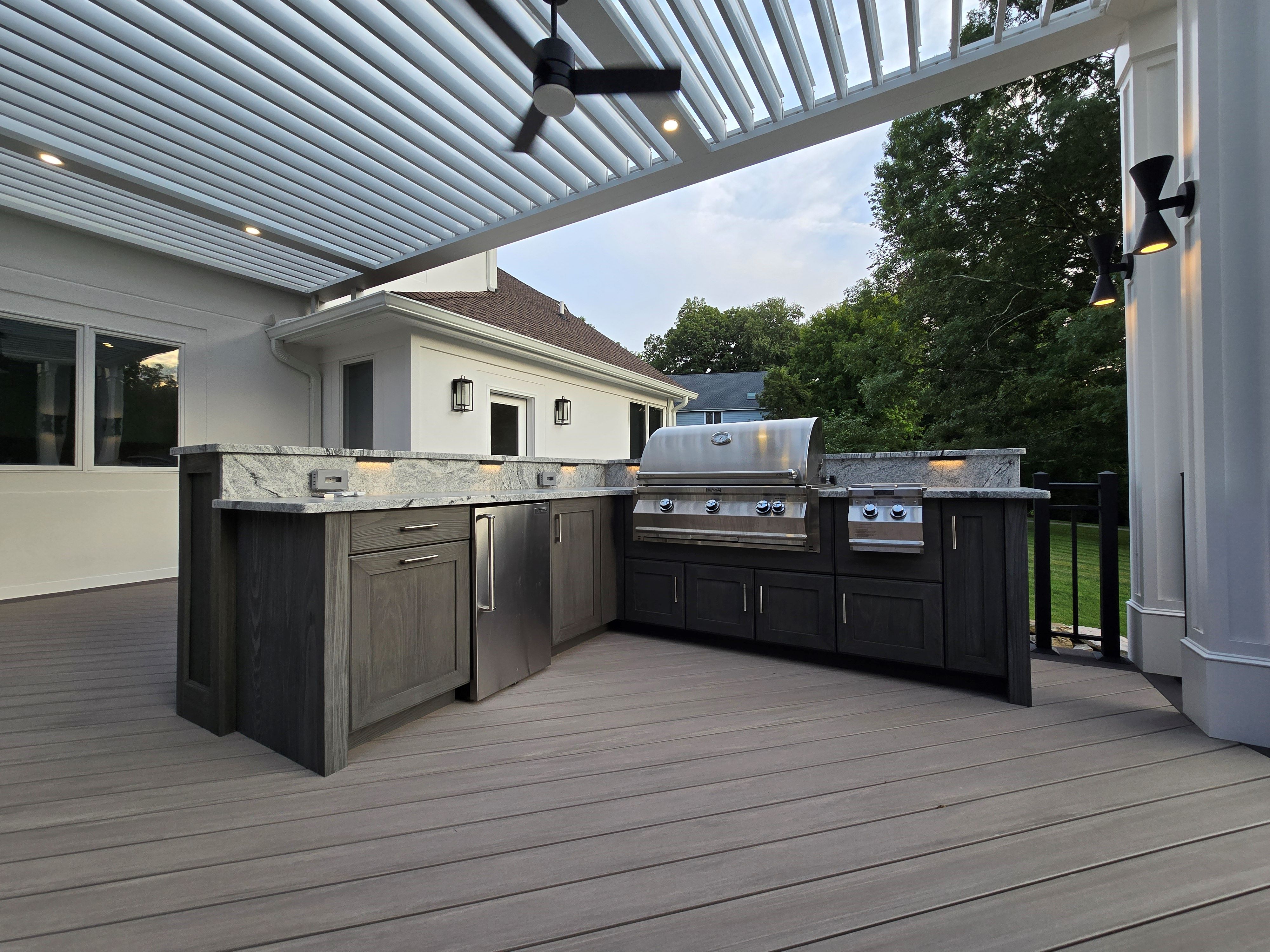 outdoor kitchen on a covered deck with granite countertops, stainless steel grill, side burner, and custom cabinetry