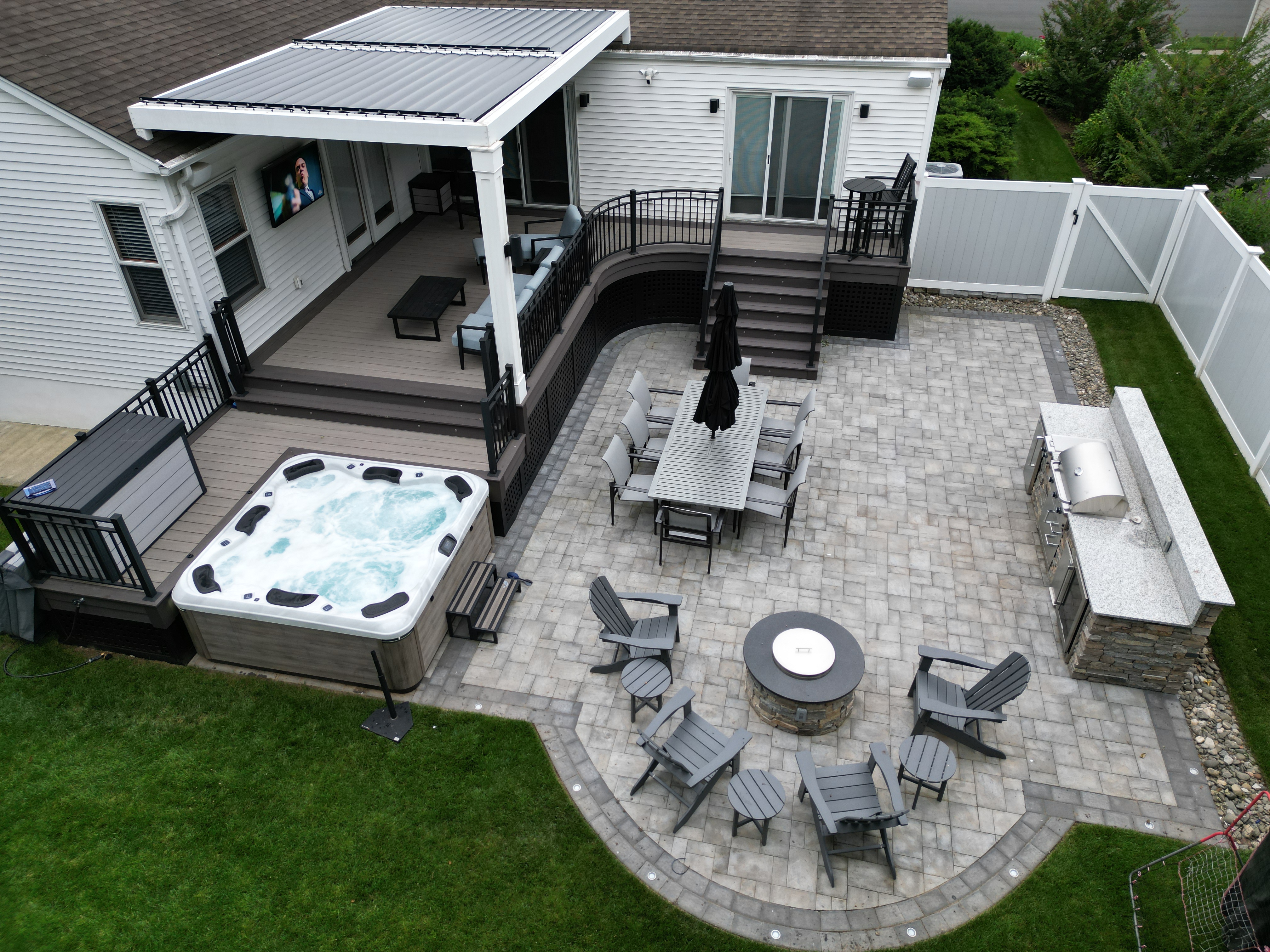 modern backyard deck design with louvered roof, hot tub, paver patio, and built-in outdoor kitchen and fire pit