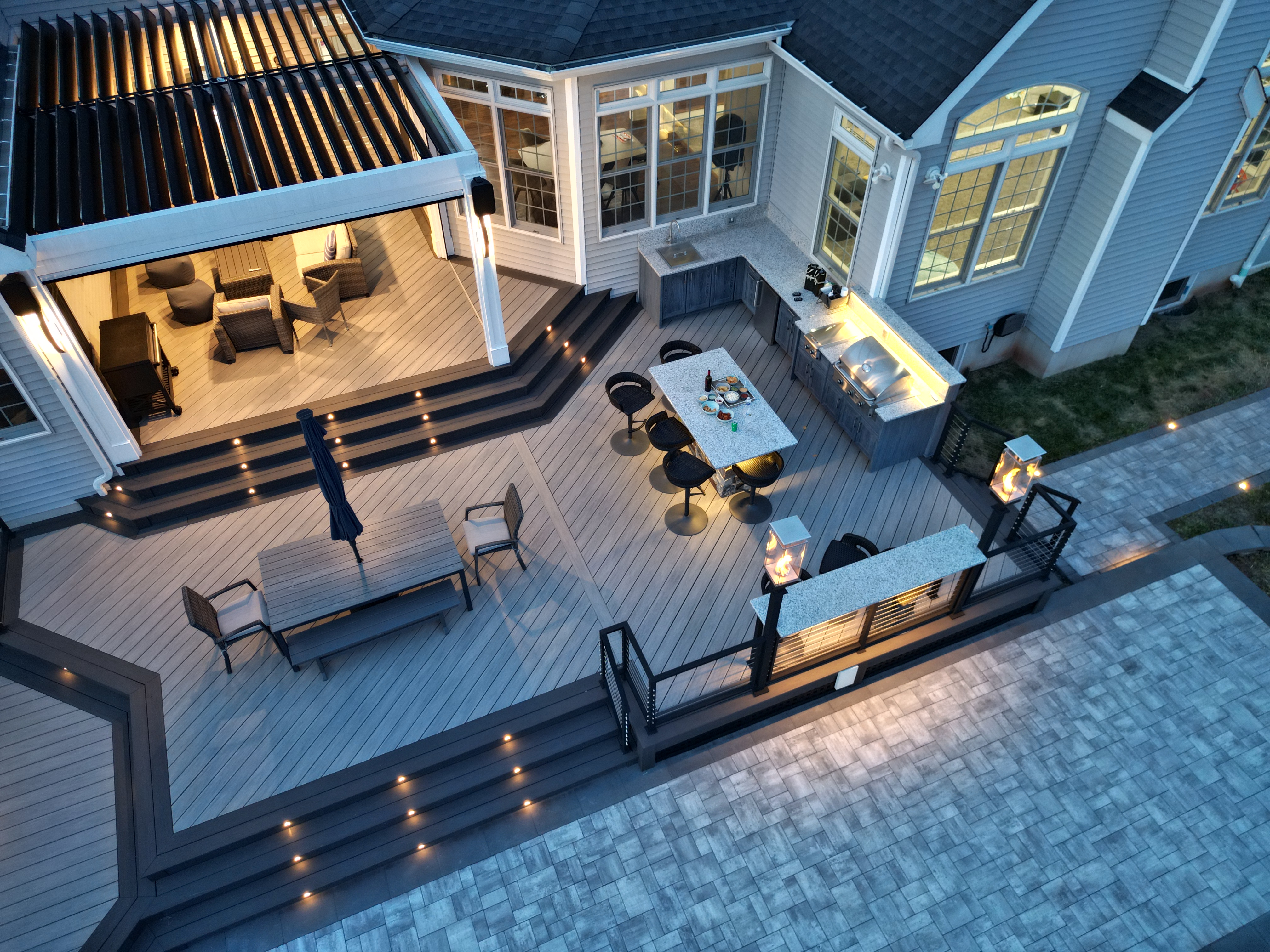 modern deck idea with outdoor kitchen, granite bar seating, louvered roof pergola, and built-in step lighting