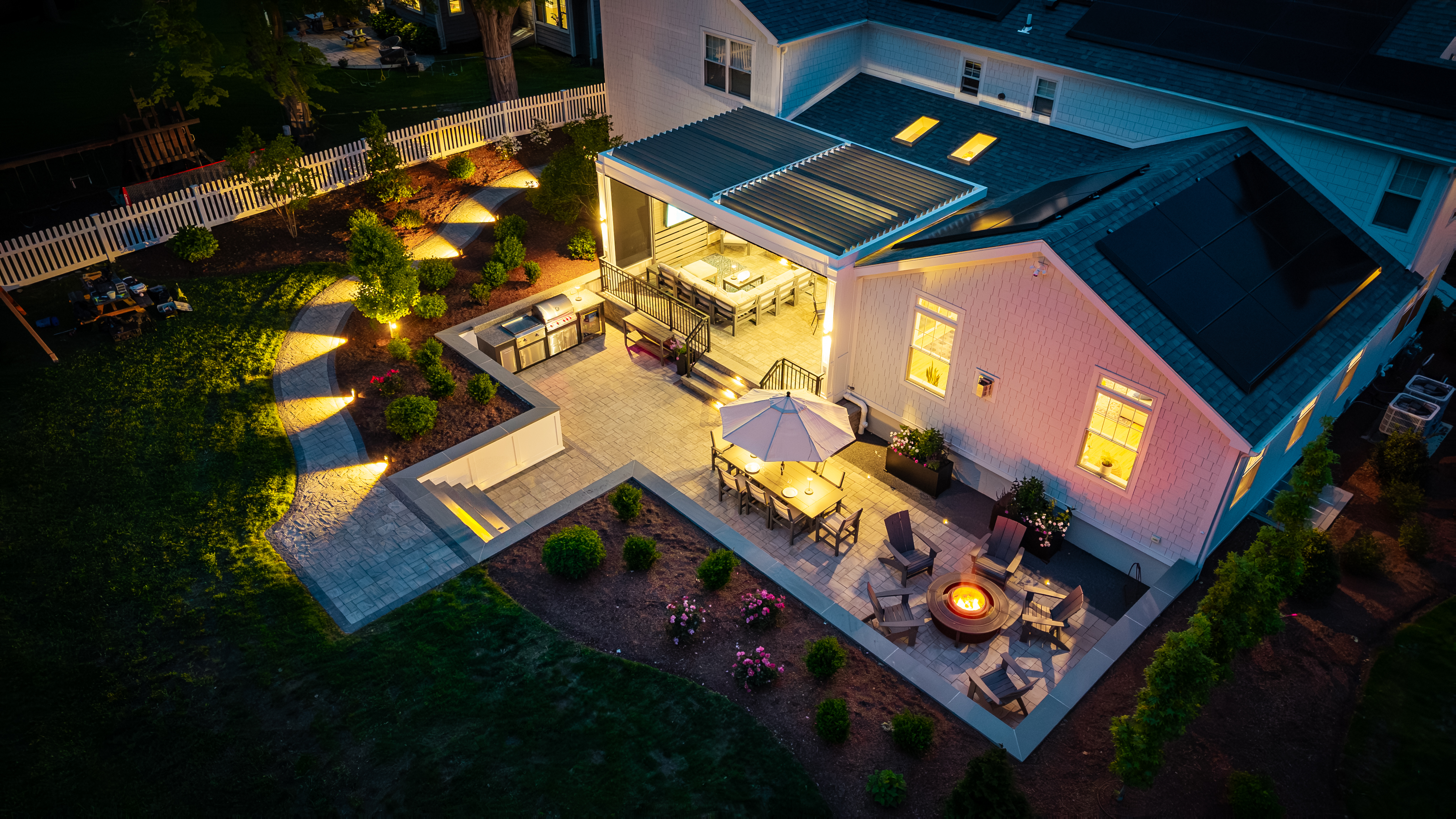 backyard sunken patio and covered deck with outdoor lighting highlighting pathways, steps, and seating areas