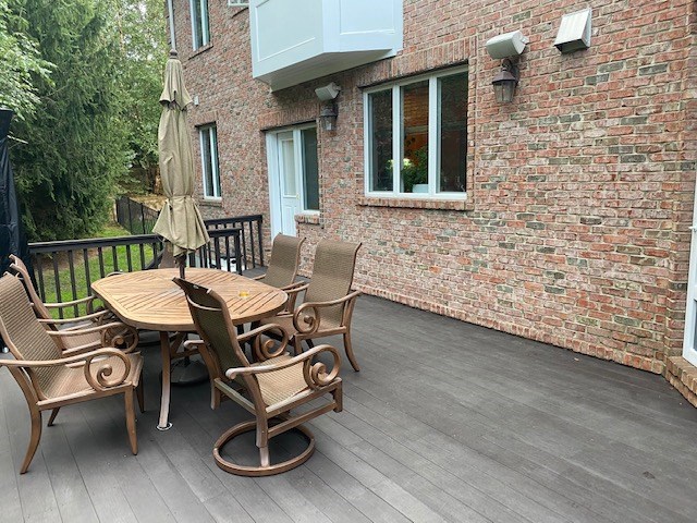 basic composite deck with dark brown decking, metal railings, and outdoor dining set against a brick exterior