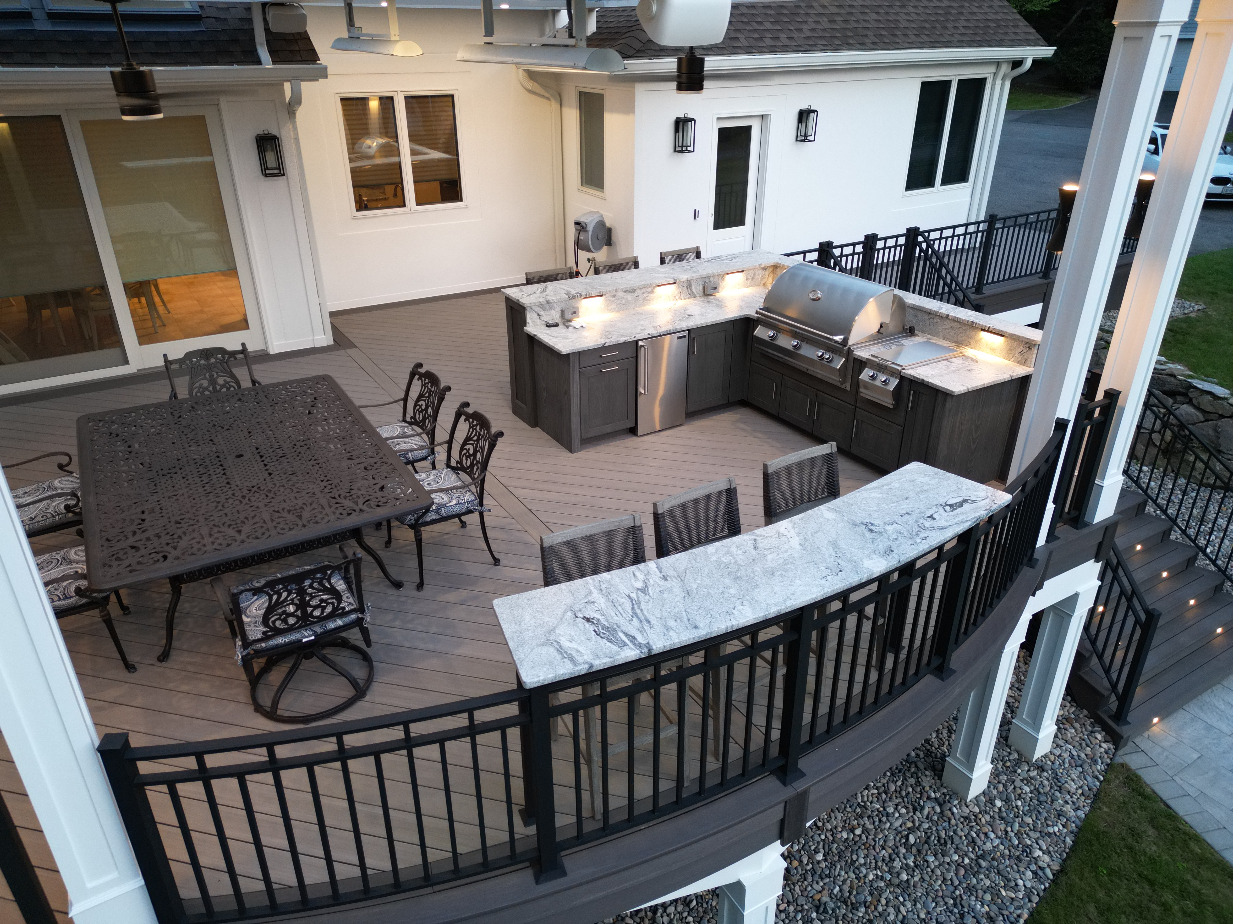 elevated deck with curved railing, custom outdoor kitchen, granite countertops, built-in grill, bar seating, and dining area on PVC decking
