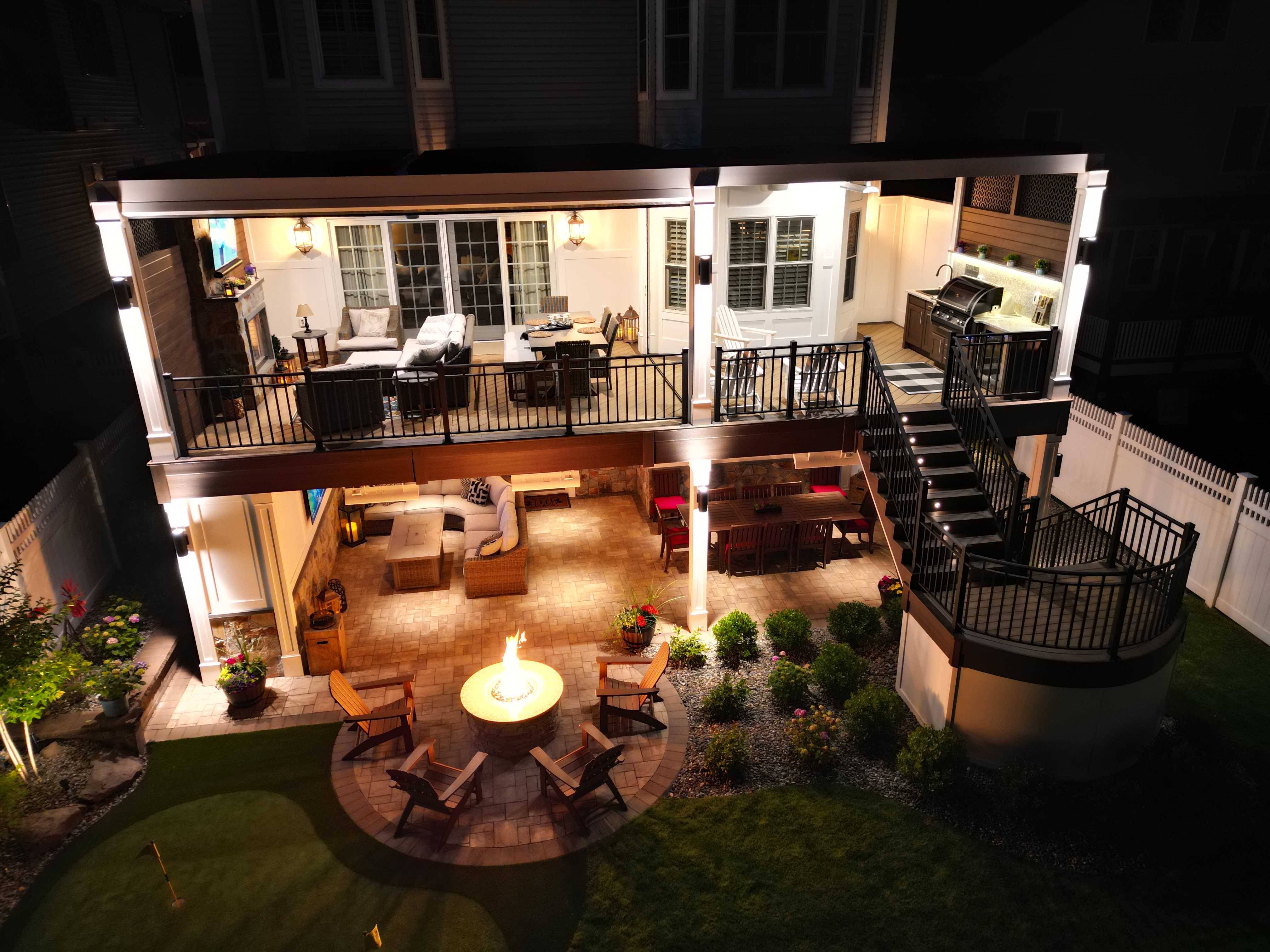 two-story deck with covered upper level, lower patio lounge, and circular fire pit seating area at night