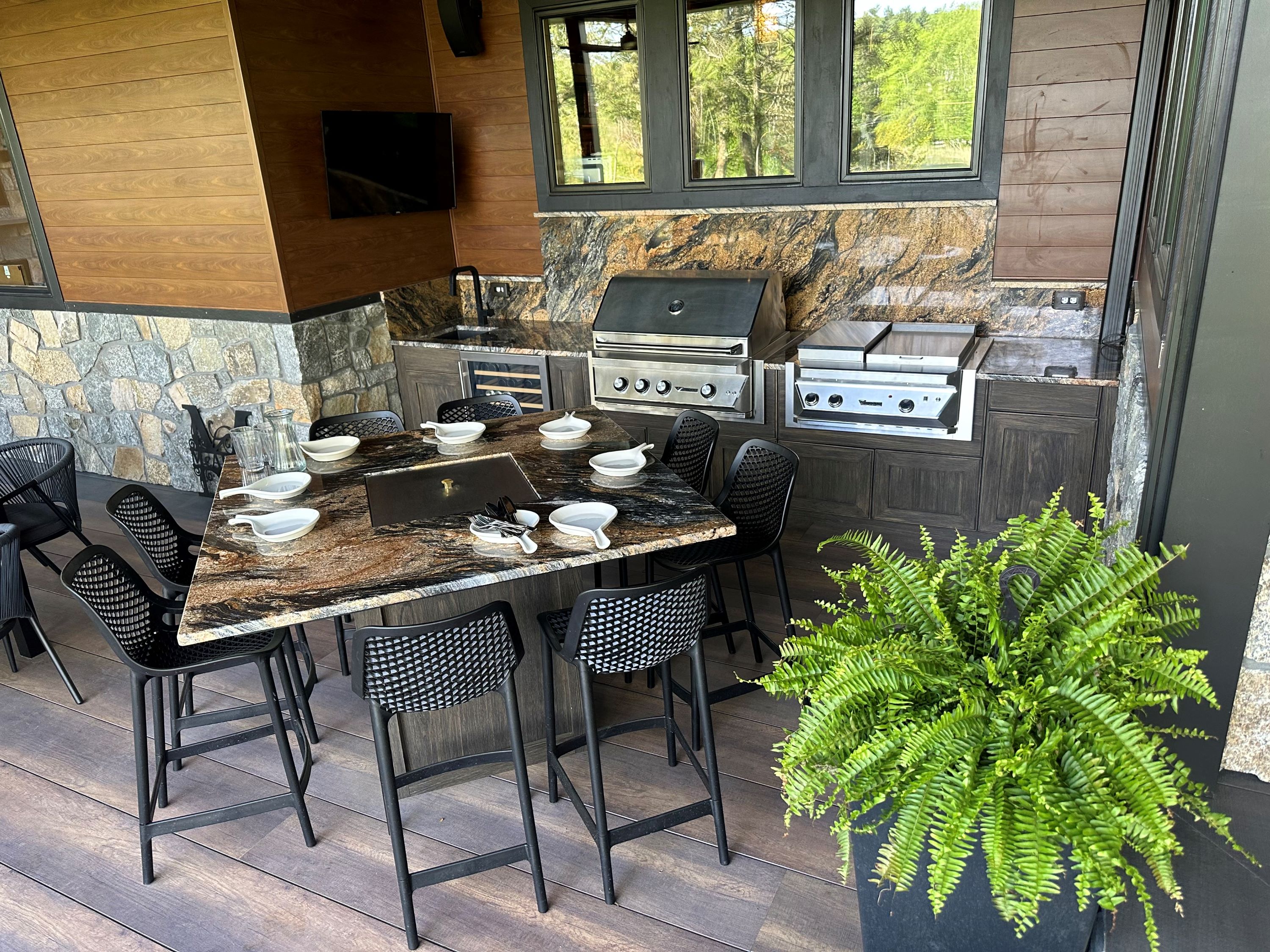 covered outdoor kitchen with built-in tabletop grill on an island, griddle, stainless steel grill, stone backsplash, and beverage refrigerator