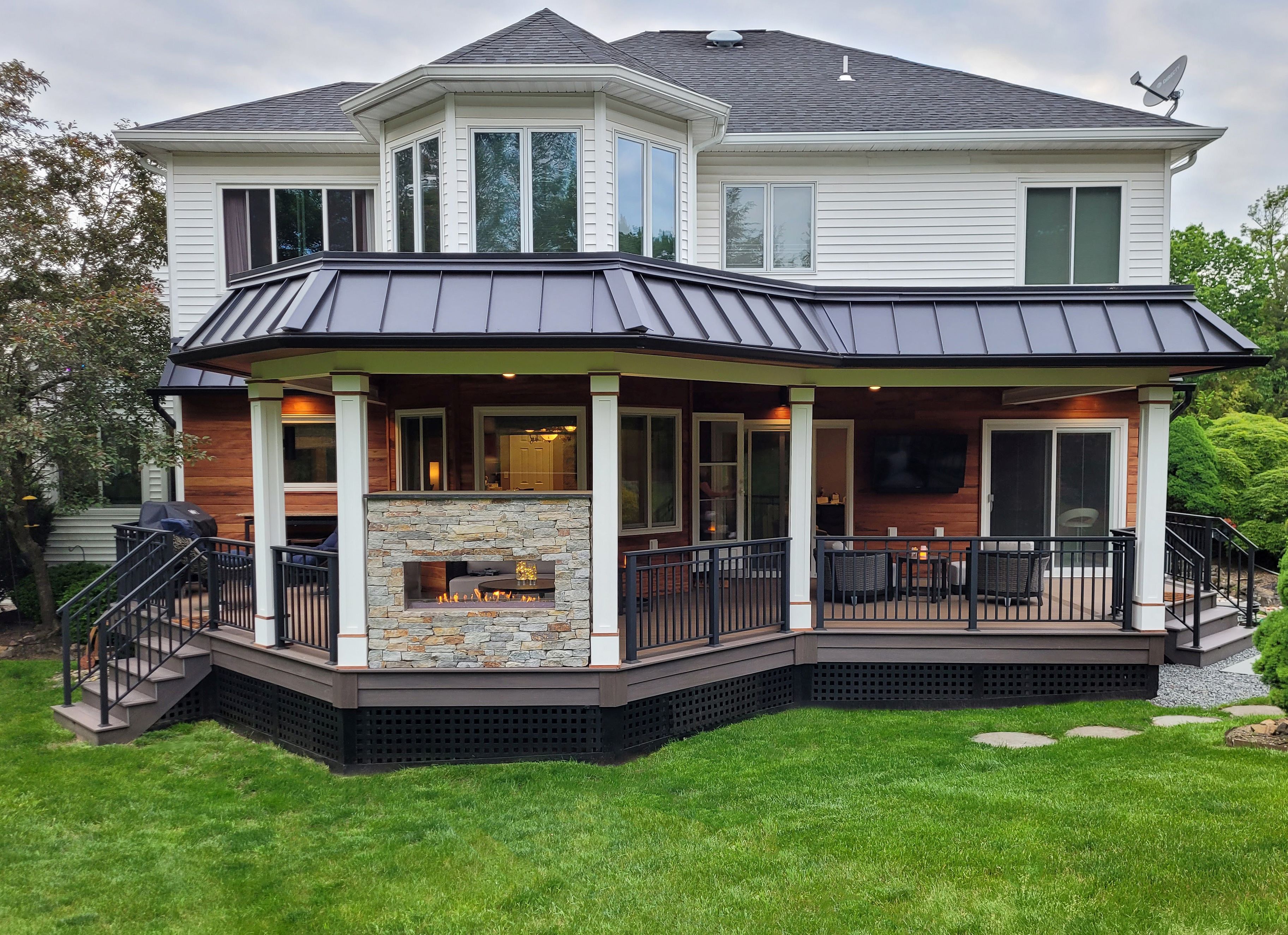 covered deck with a roof extension, double-sided stone fireplace, and outdoor seating area