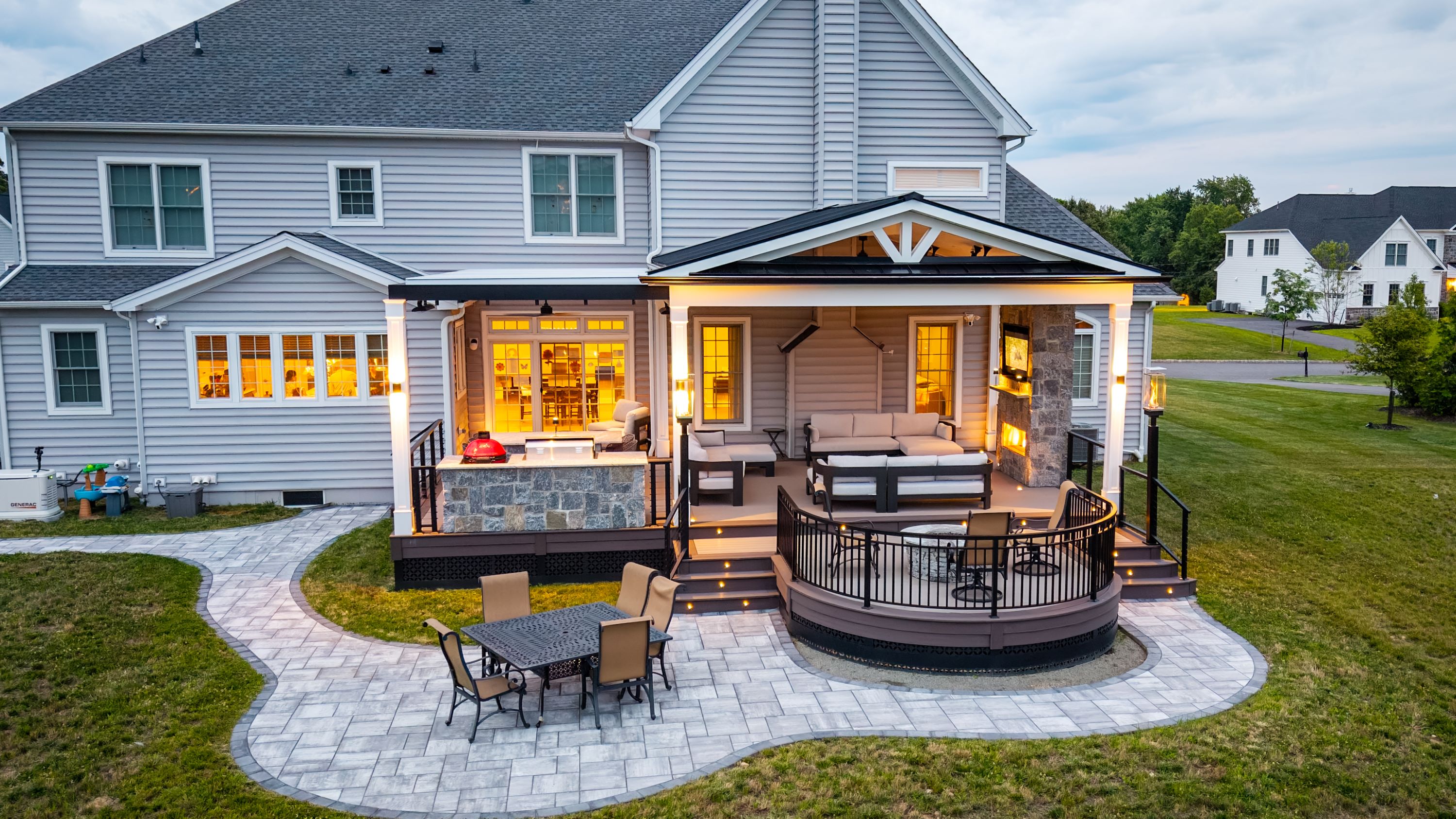 multi-level deck with covered lounge, stone fireplace, outdoor kitchen, curved fire pit level, and paver patio with dining set