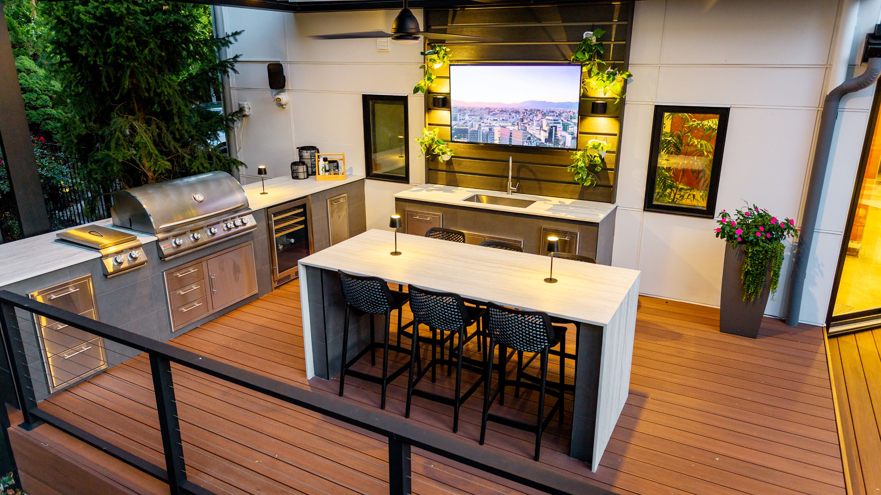 modern outdoor kitchen on a deck with built-in grill, sink, refrigerator, bar seating, outdoor television, and integrated lighting