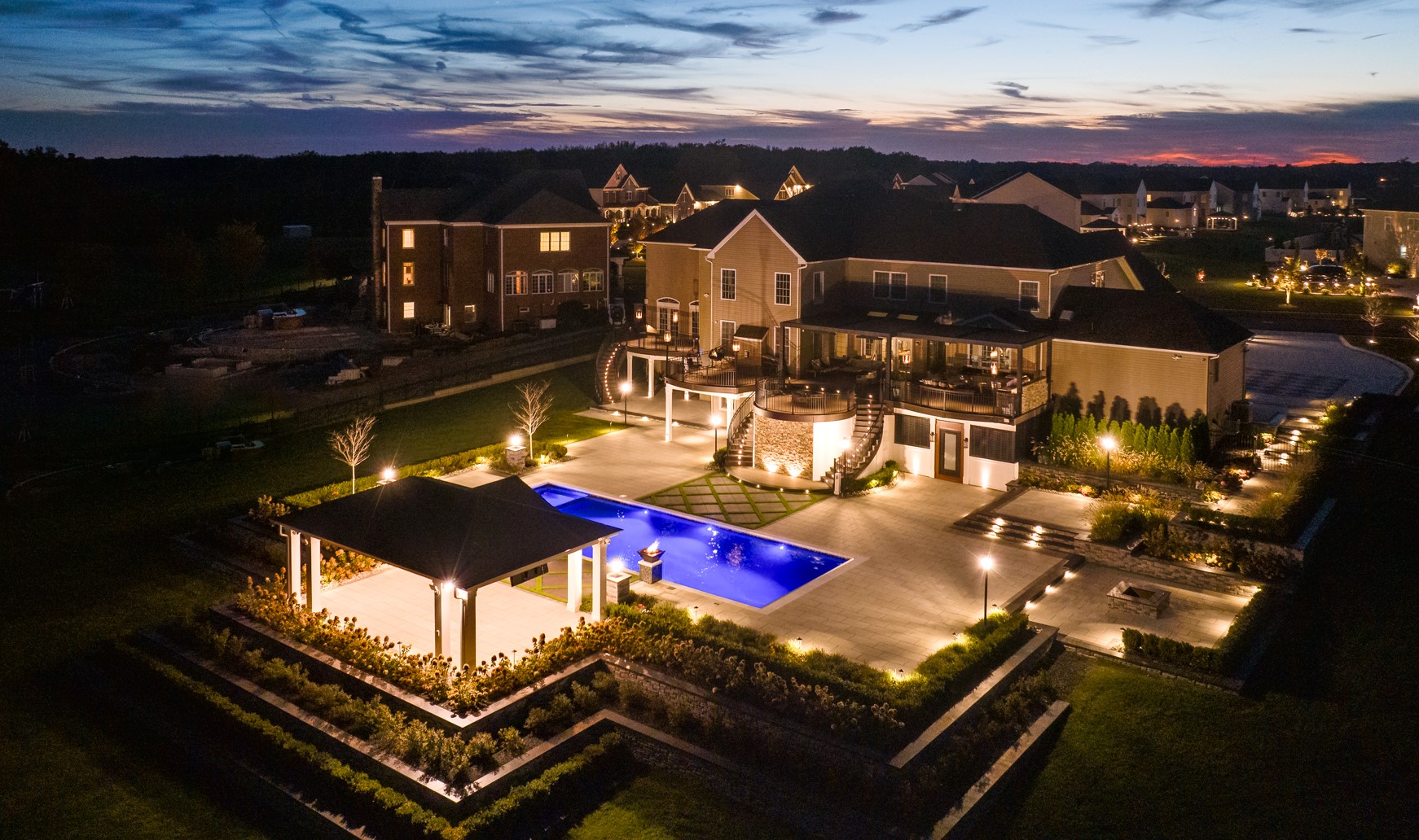 aerial view of illuminated backyard with pool, paver patio, and multi-level deck at dusk