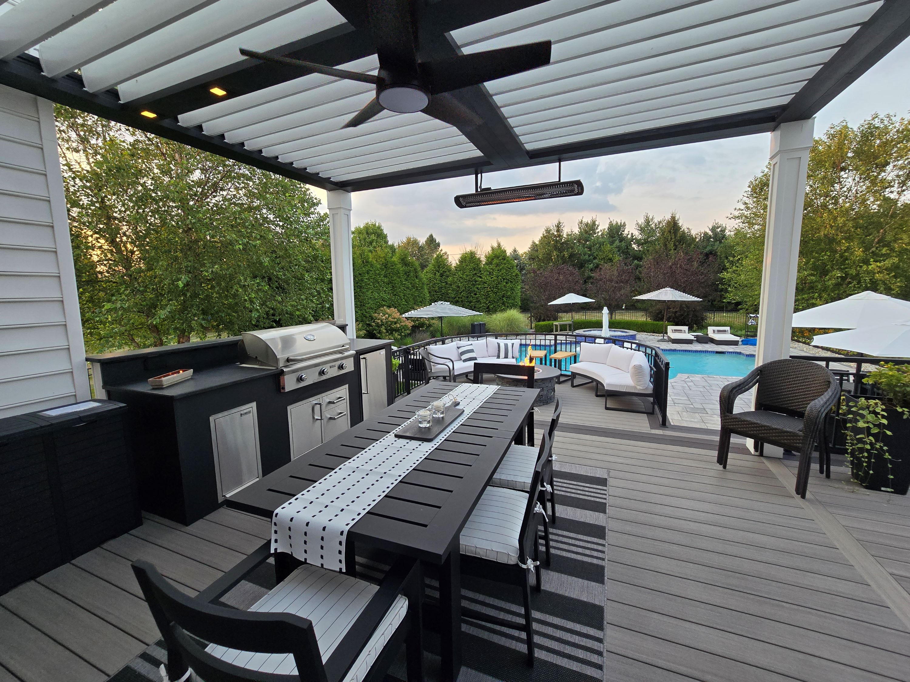 covered deck with outdoor kitchen, dining table, lounge seating, and pool view