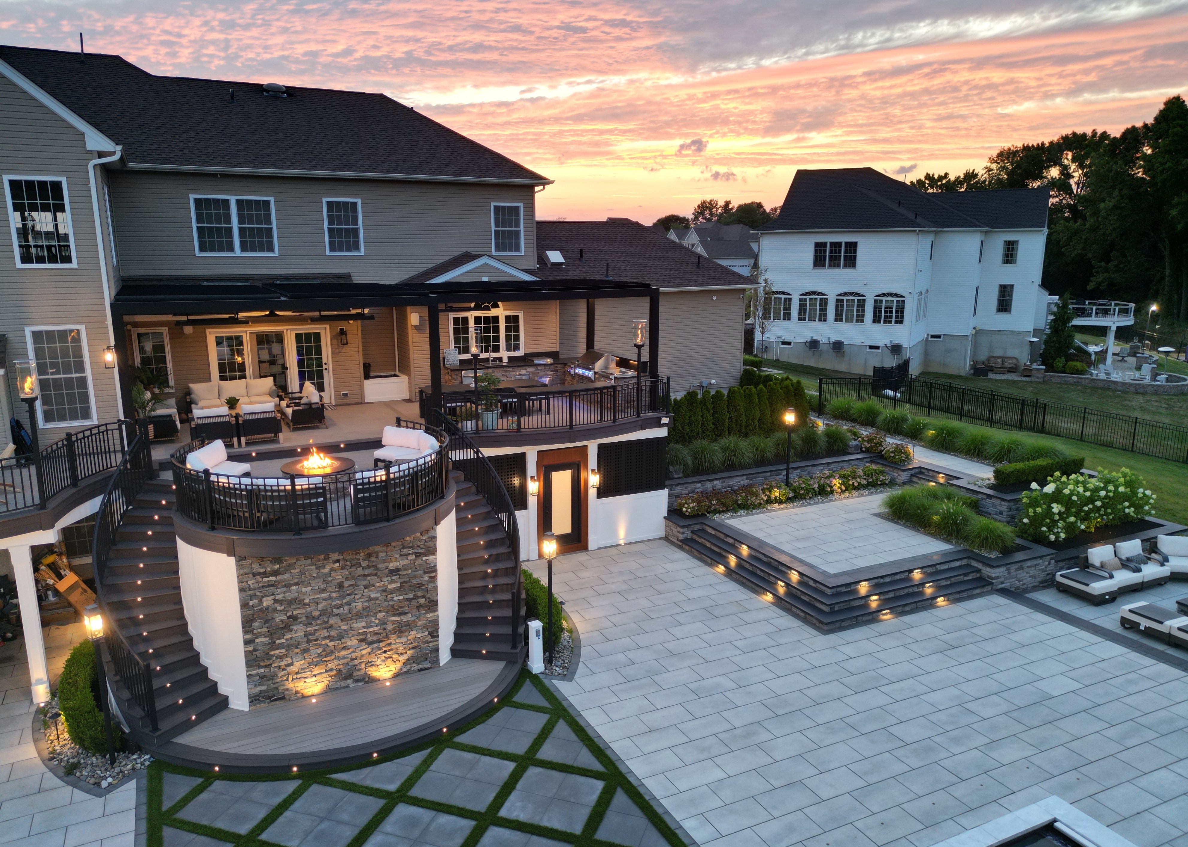 multi-level deck and patio with curved double staircase, elevated fire pit lounge, louvered roof pergola, hot tub, and expansive tiered hardscaping