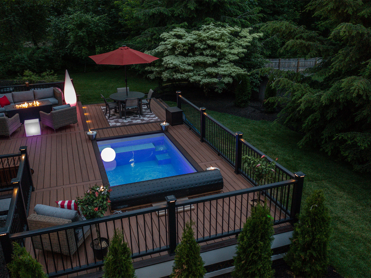 small plunge pool built into a deck with surrounding seating, dining area, and railing in a private backyard setting