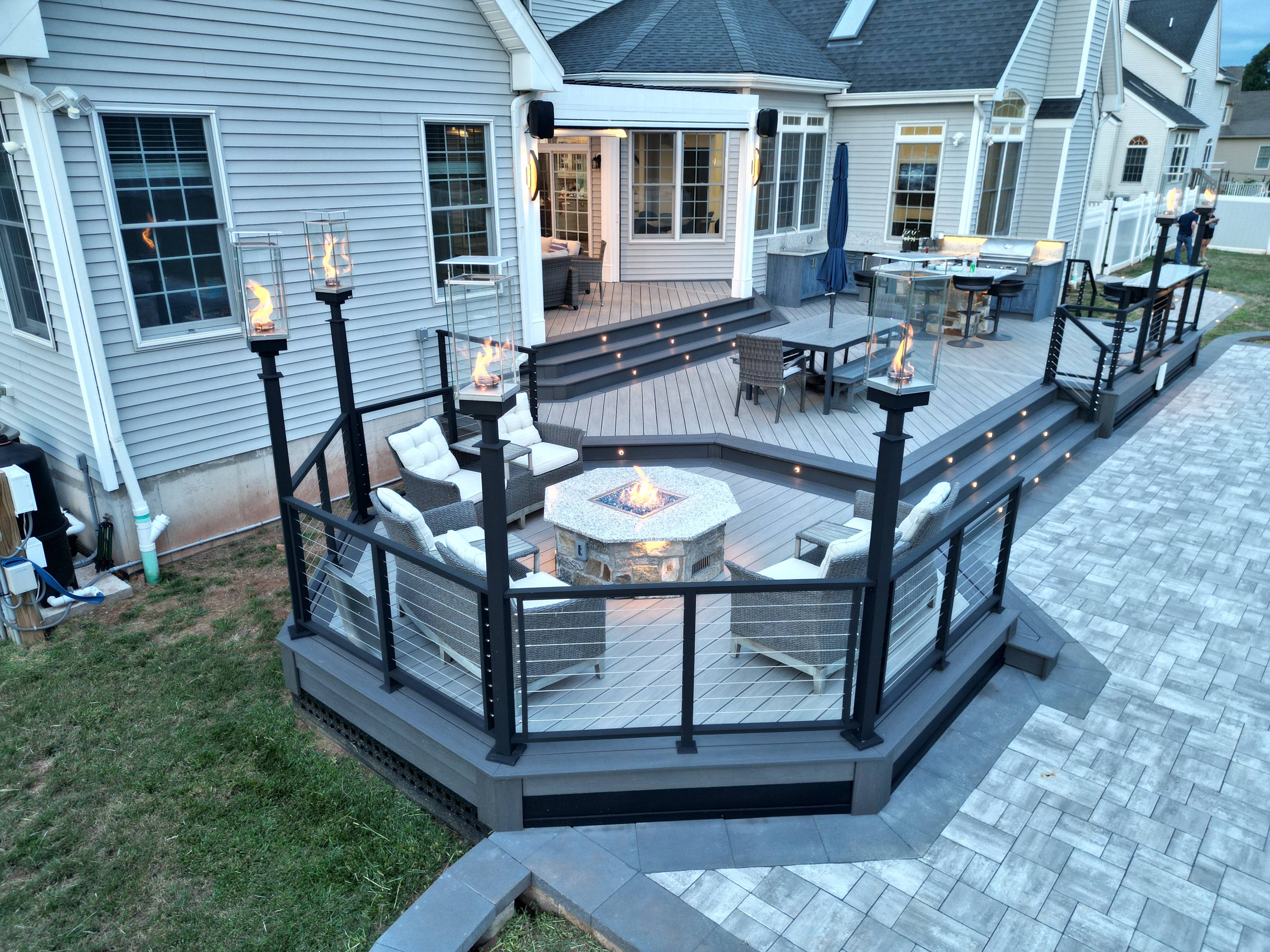 spacious deck with white louvered roof, outdoor kitchen with bar seating, dining area, and step lighting