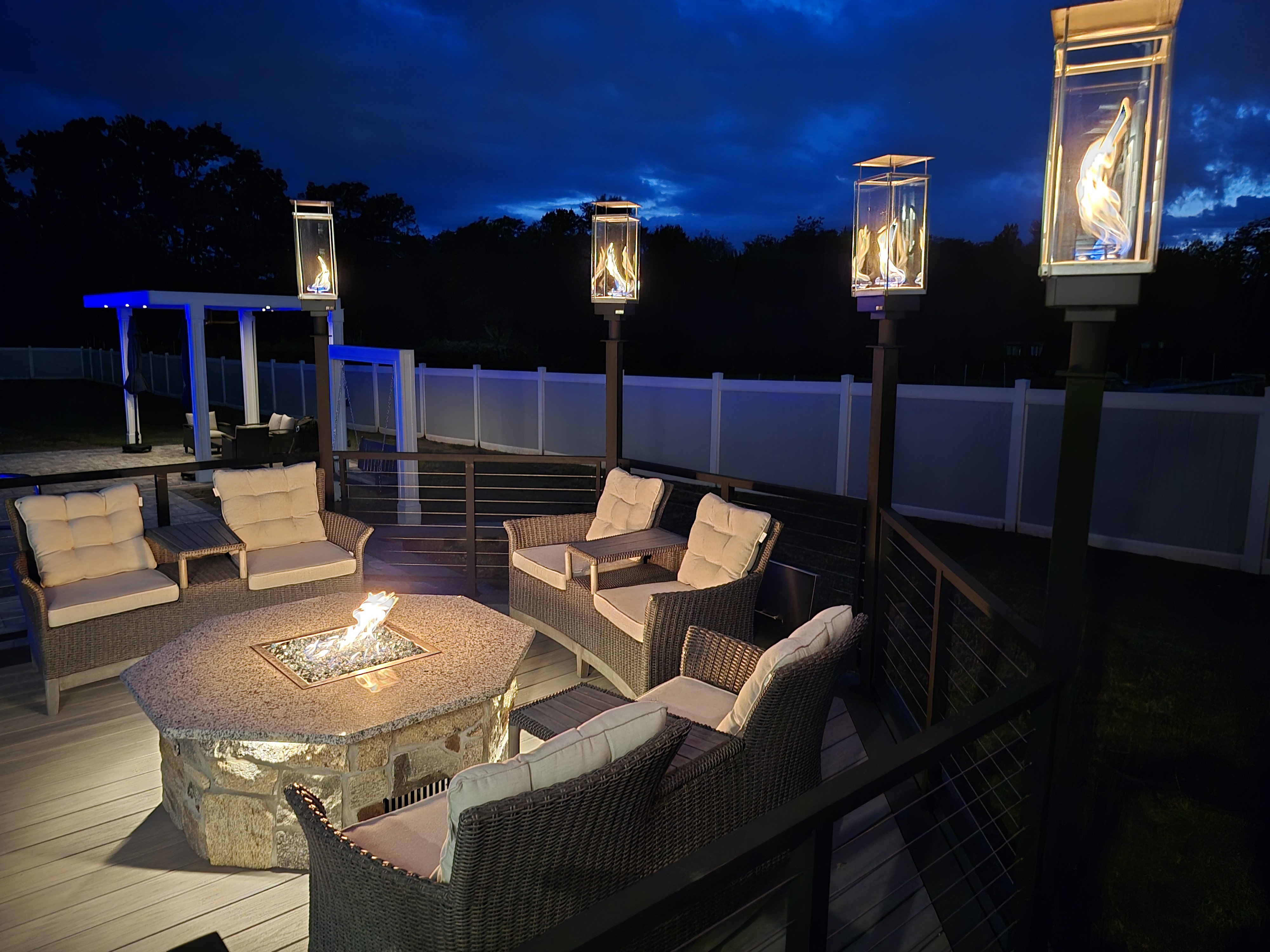 outdoor fire pit seating area with wicker chairs, stone fire table, and gas lantern deck lighting at night