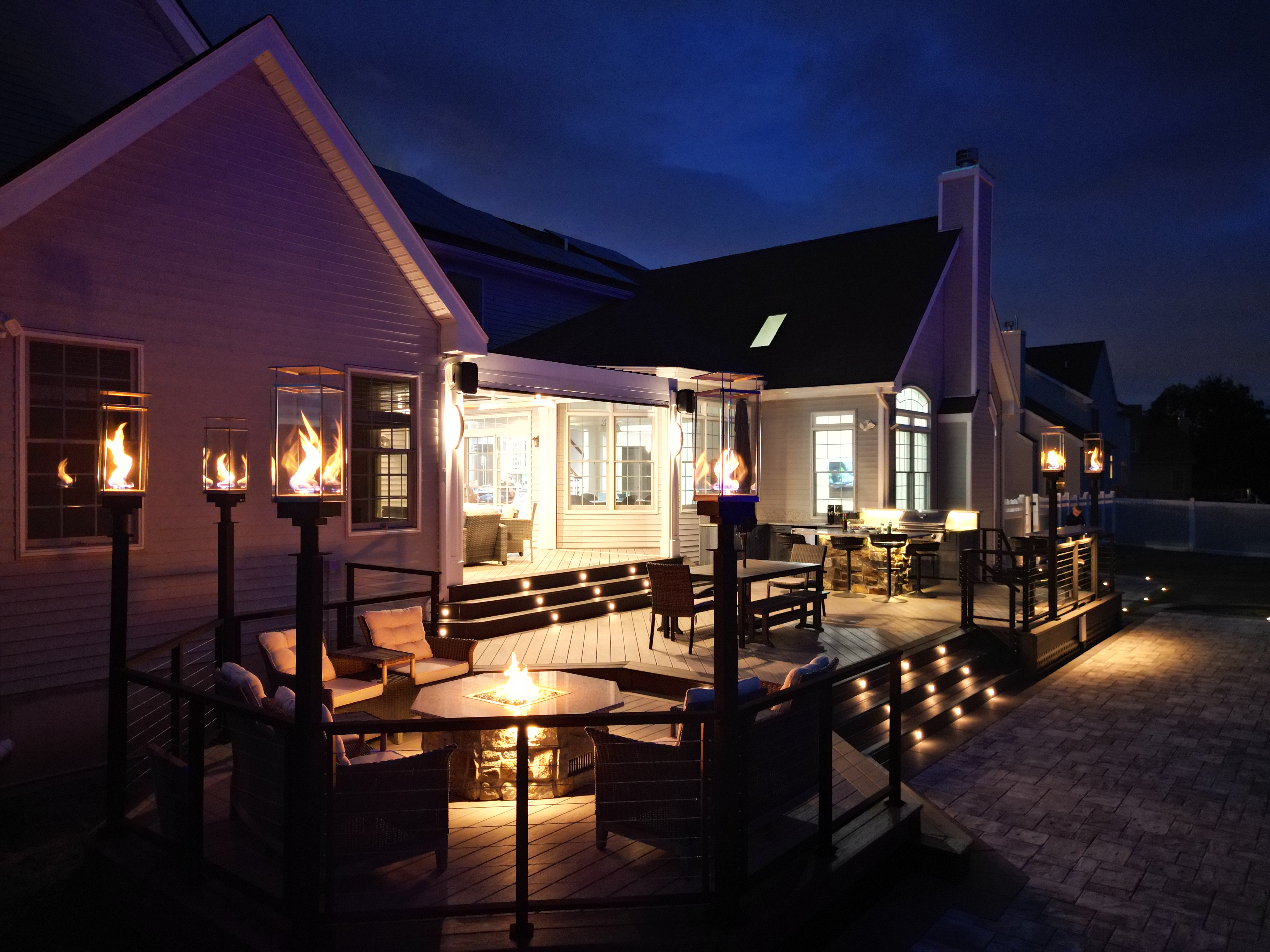 multi-level deck at night with built-in fire pit, seating area, and integrated step and post lighting