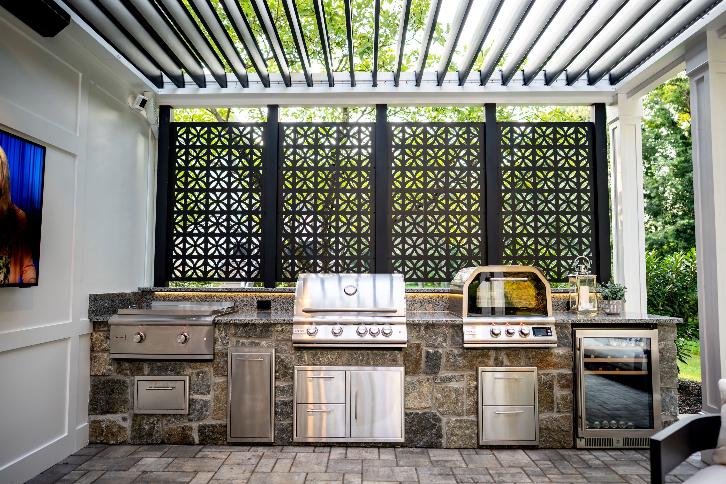 covered outdoor kitchen with built-in grill, griddle, pizza oven, metal cabinetry, wine refrigerator, and decorative privacy wall