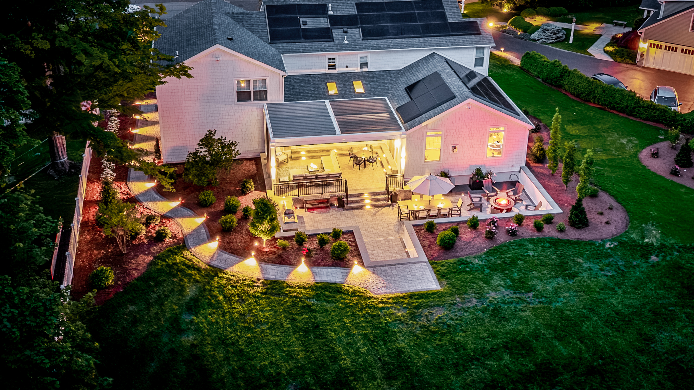backyard with integrated landscape lighting illuminating pathways, patio seating areas, and fire pit at dusk