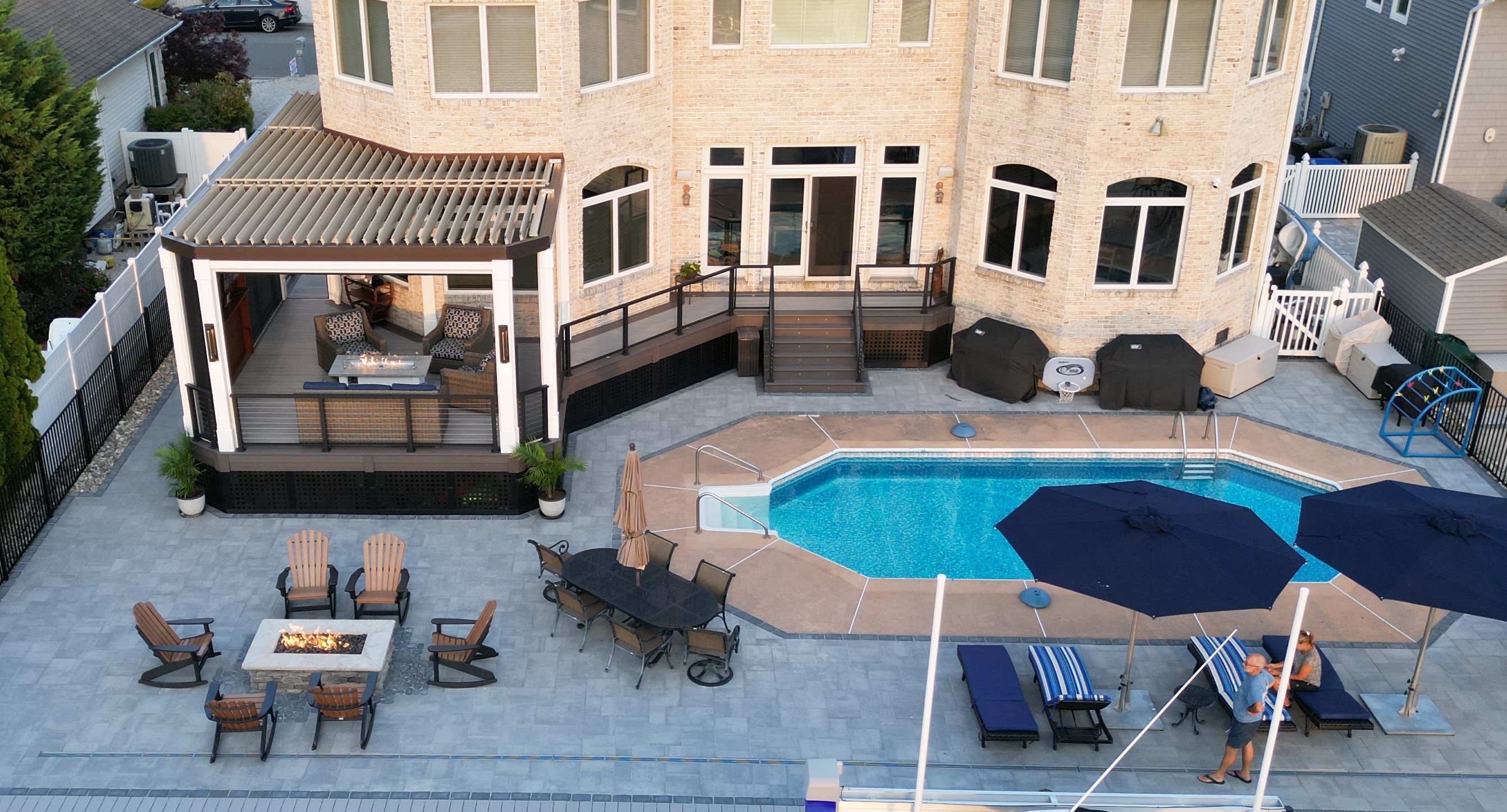 backyard outdoor living space with covered lounge structure, poolside umbrellas, dining area, and fire pit seating