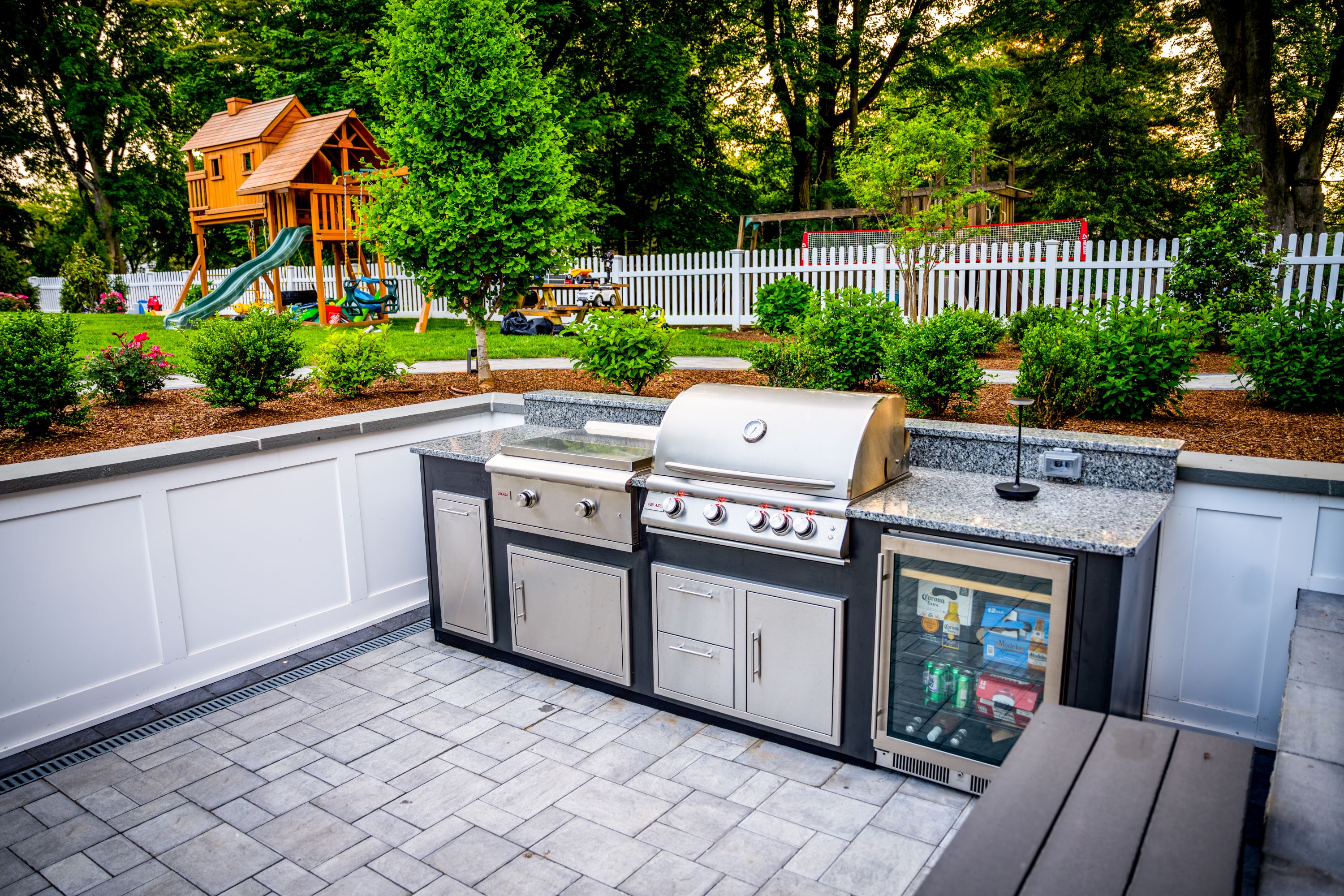 sunken patio outdoor kitchen with built-in grill, griddle, beverage refrigerator, stone pavers, and white retaining walls