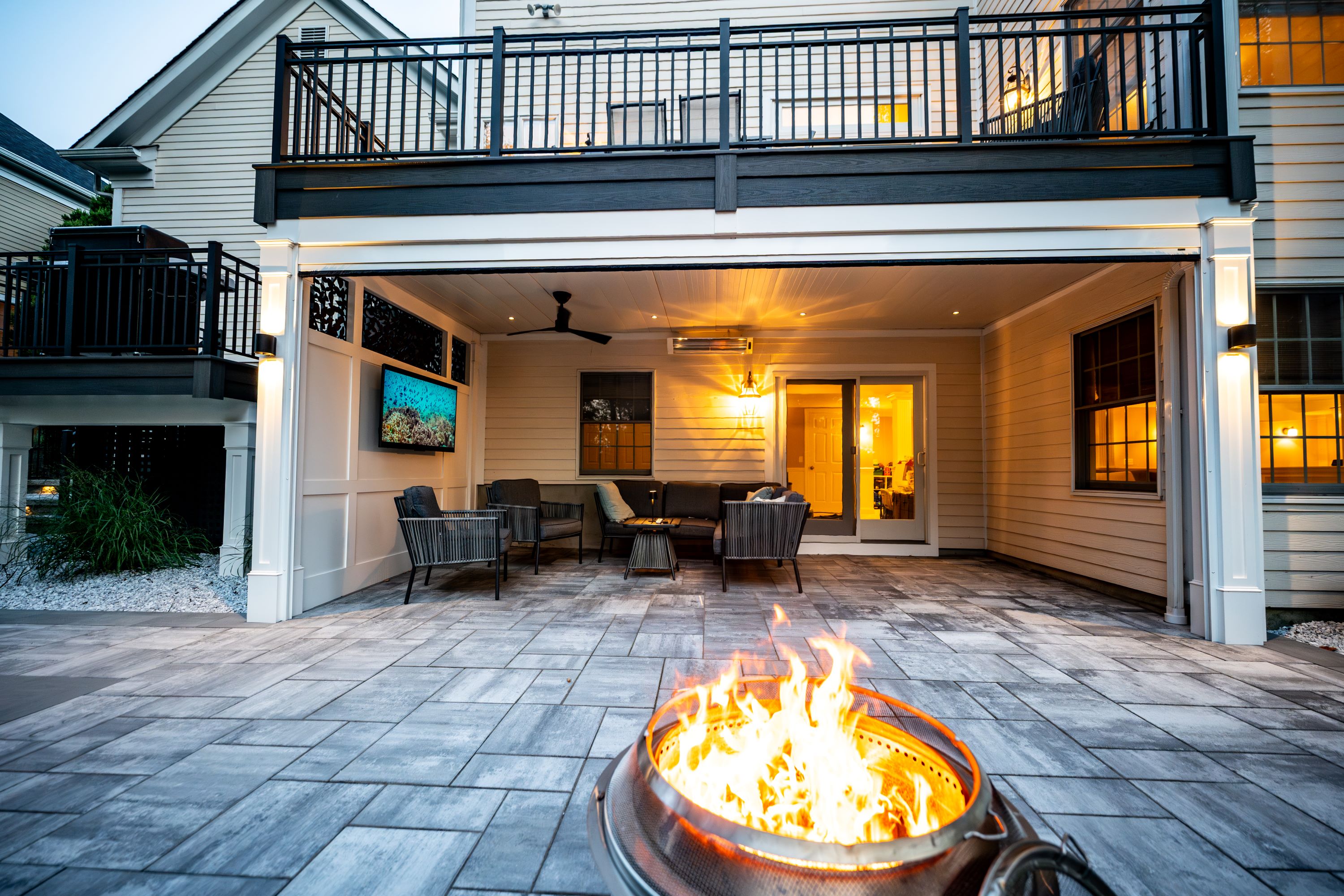 finished under deck lounge area with tongue-and-groove ceiling, recessed lighting, ceiling fan, wall-mounted TV, infrared heater, and lounge seating opening to a paver patio with fire pit