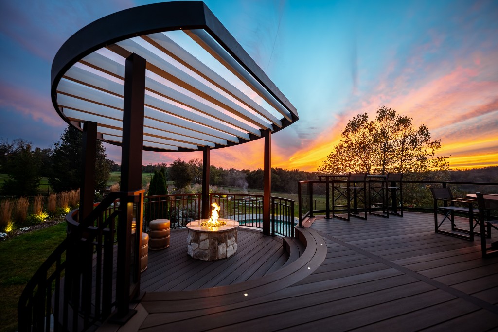 Modern deck with curved louvered roof and fire pit overlooking a pool scenic sunset, Made by Deck Remodelers