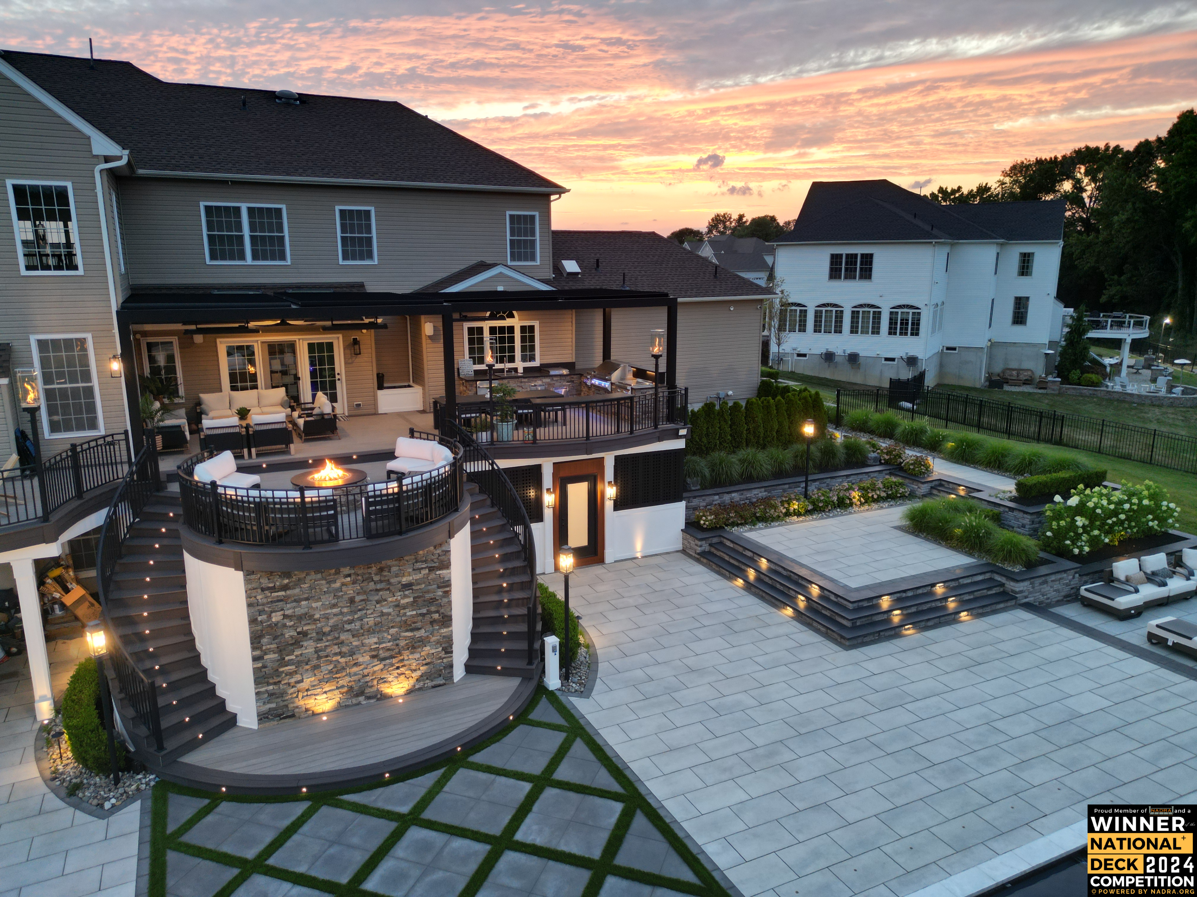 award-winning multi-level deck with louvered roof, curved fire pit lounge, spiral staircase, stone accents, and expansive paver patio with tiered landscaping