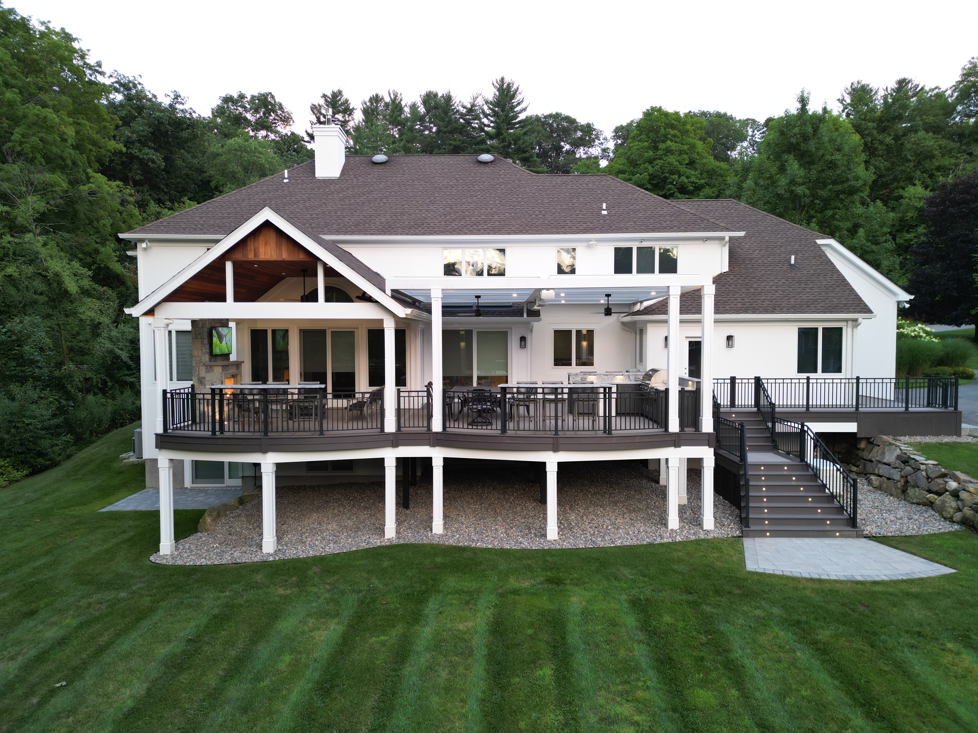 elevated deck with black railings, covered outdoor kitchen, lounge seating, and wide staircase leading to the yard