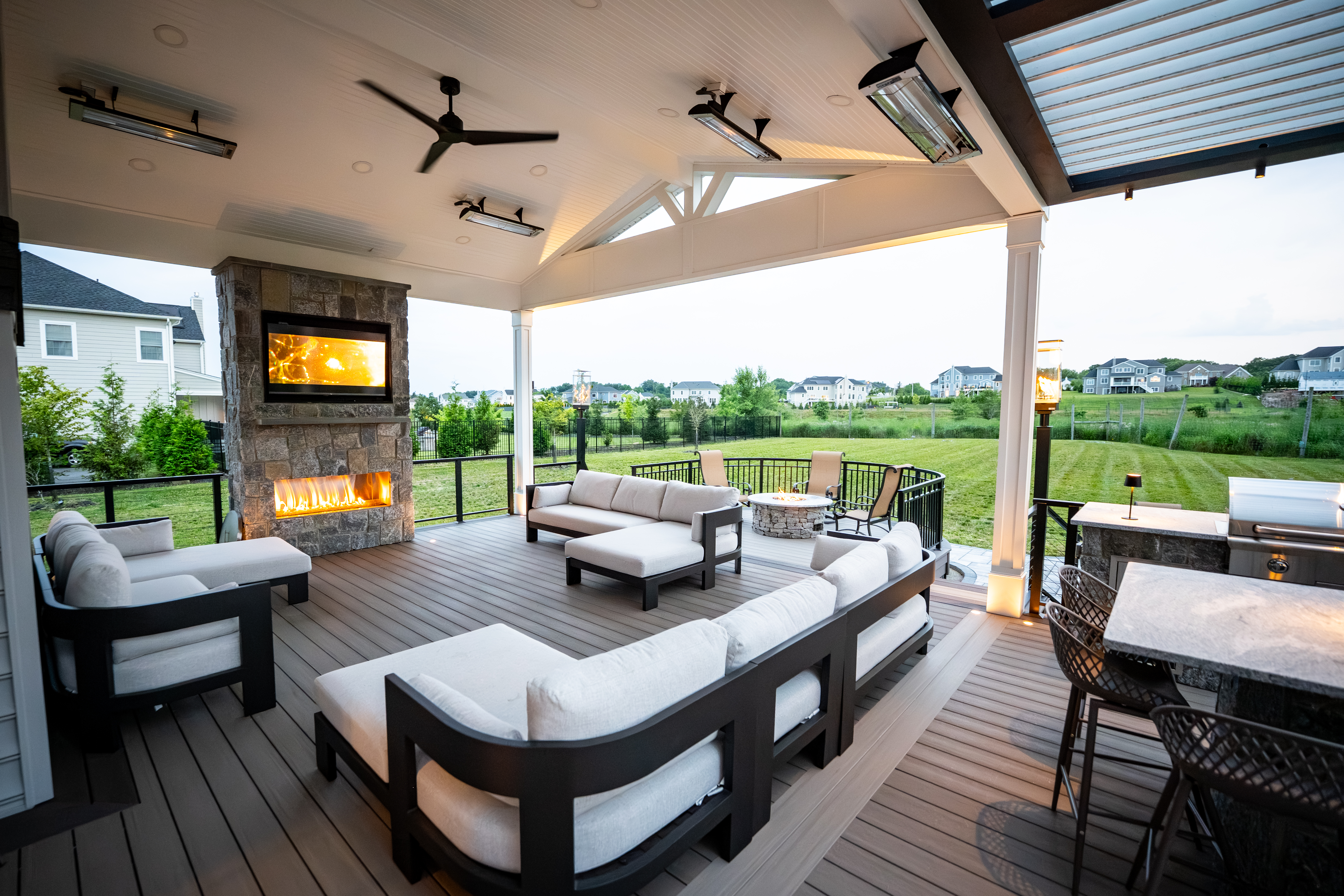 covered outdoor living area with stone fireplace, ceiling heaters, built-in grill station, curved fire pit lounge, and cushioned sectional seating