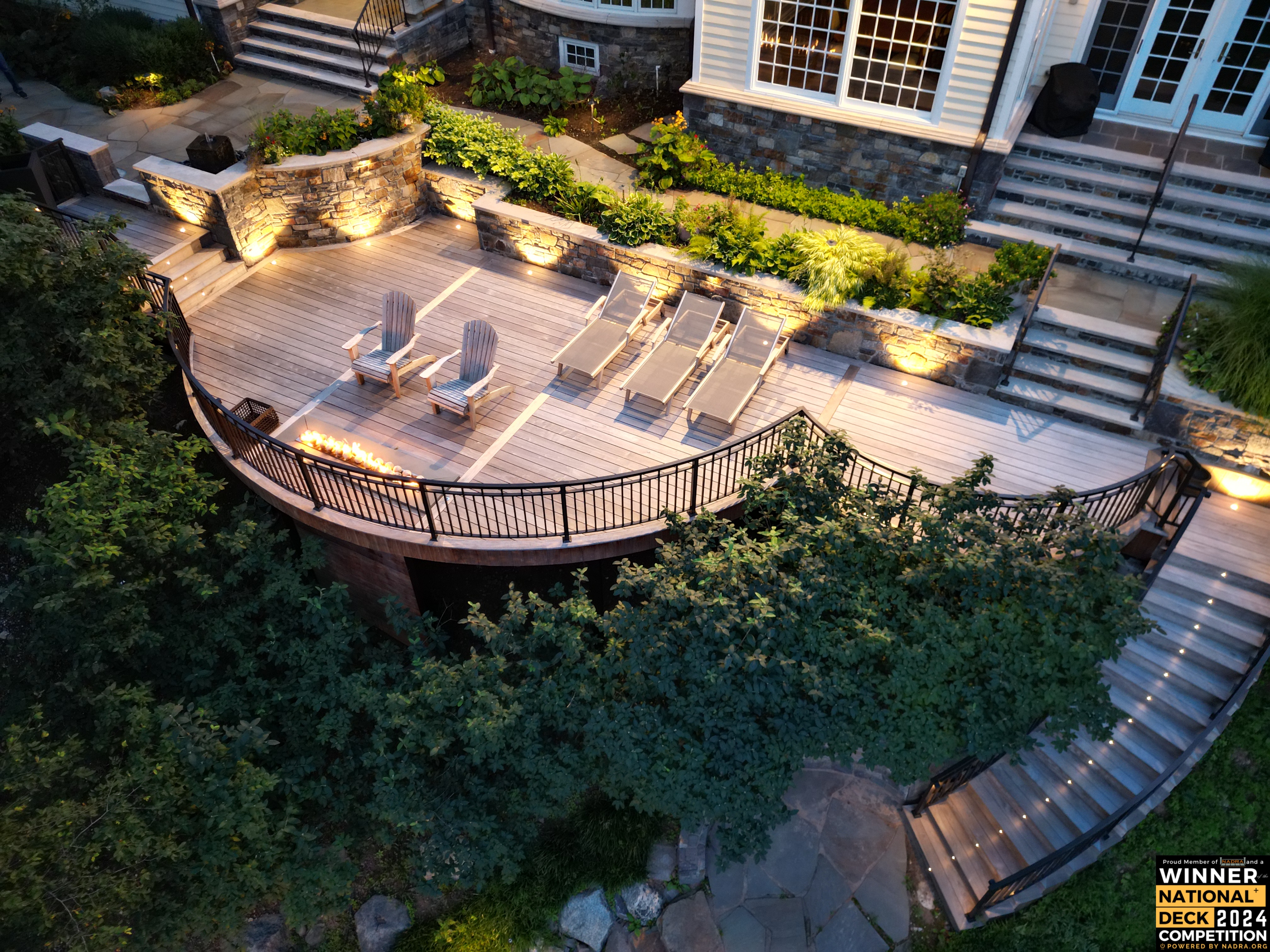 award-winning curved wood deck with built-in fire feature, accent lighting, curved stairs, and terraced stone retaining walls