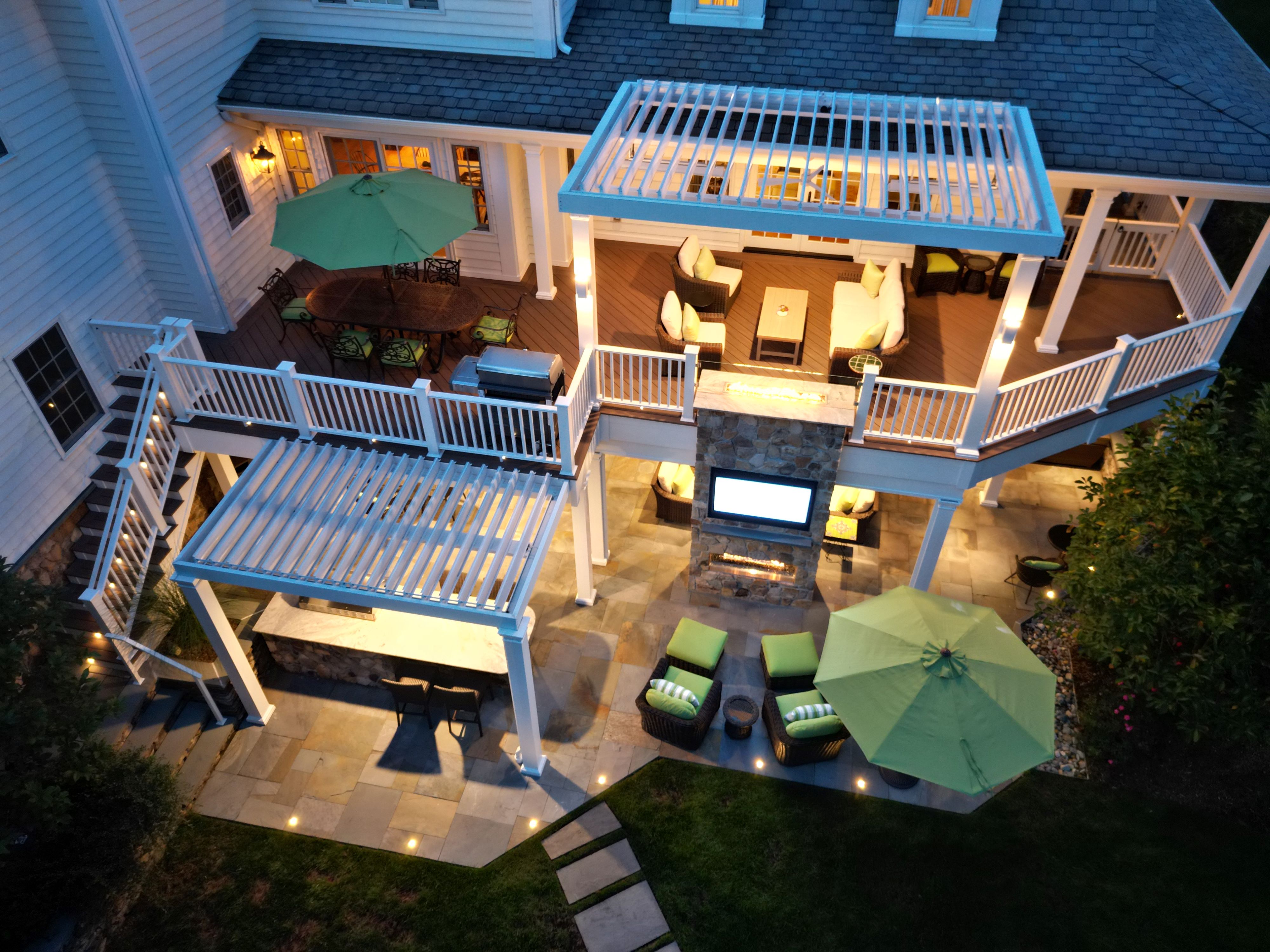 multi-level outdoor living space with covered deck lounge, patio seating areas, fireplace feature wall, and outdoor bar area