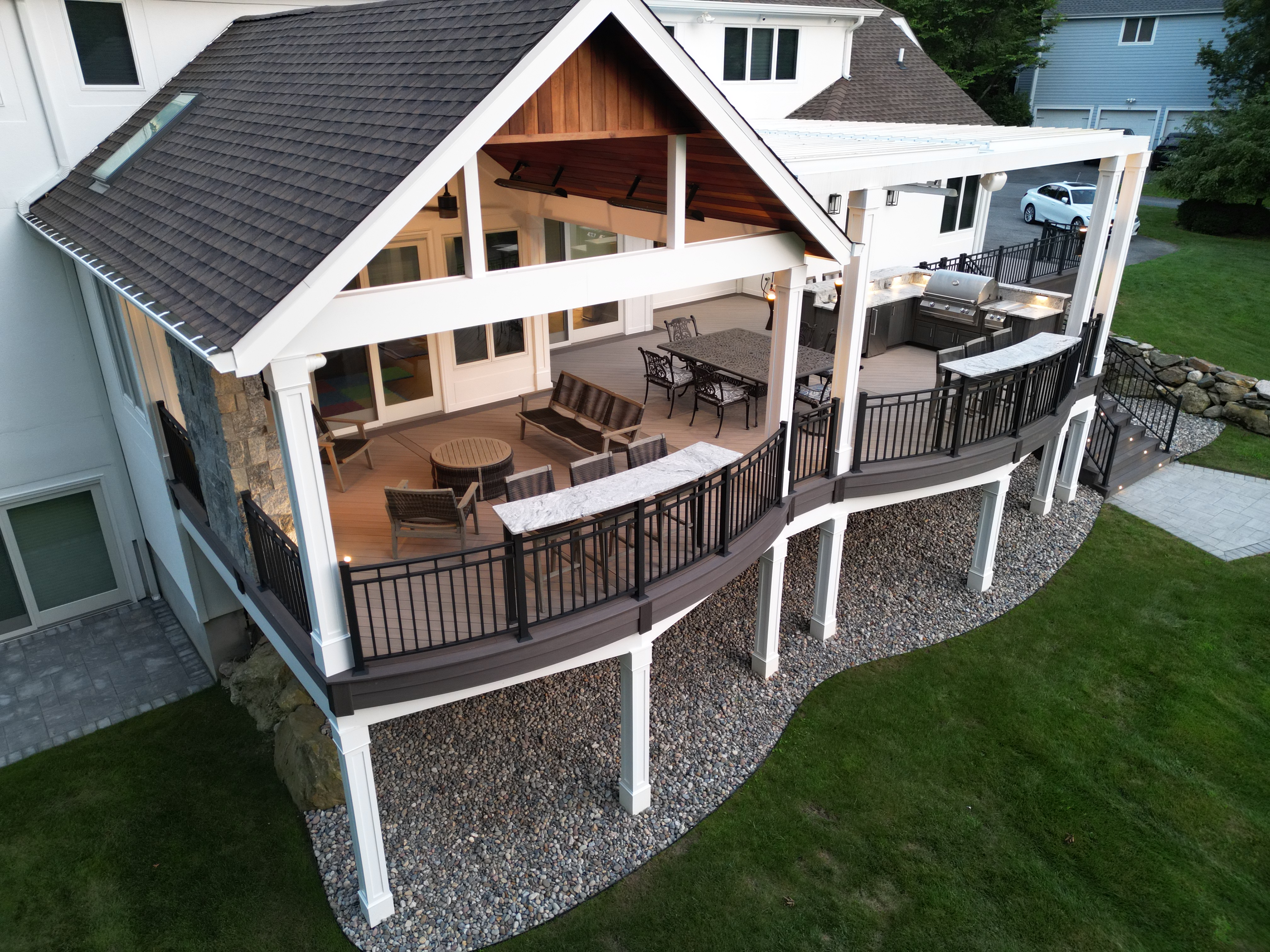 elevated covered deck with vaulted roof, dining area, and curved railing overlooking backyard