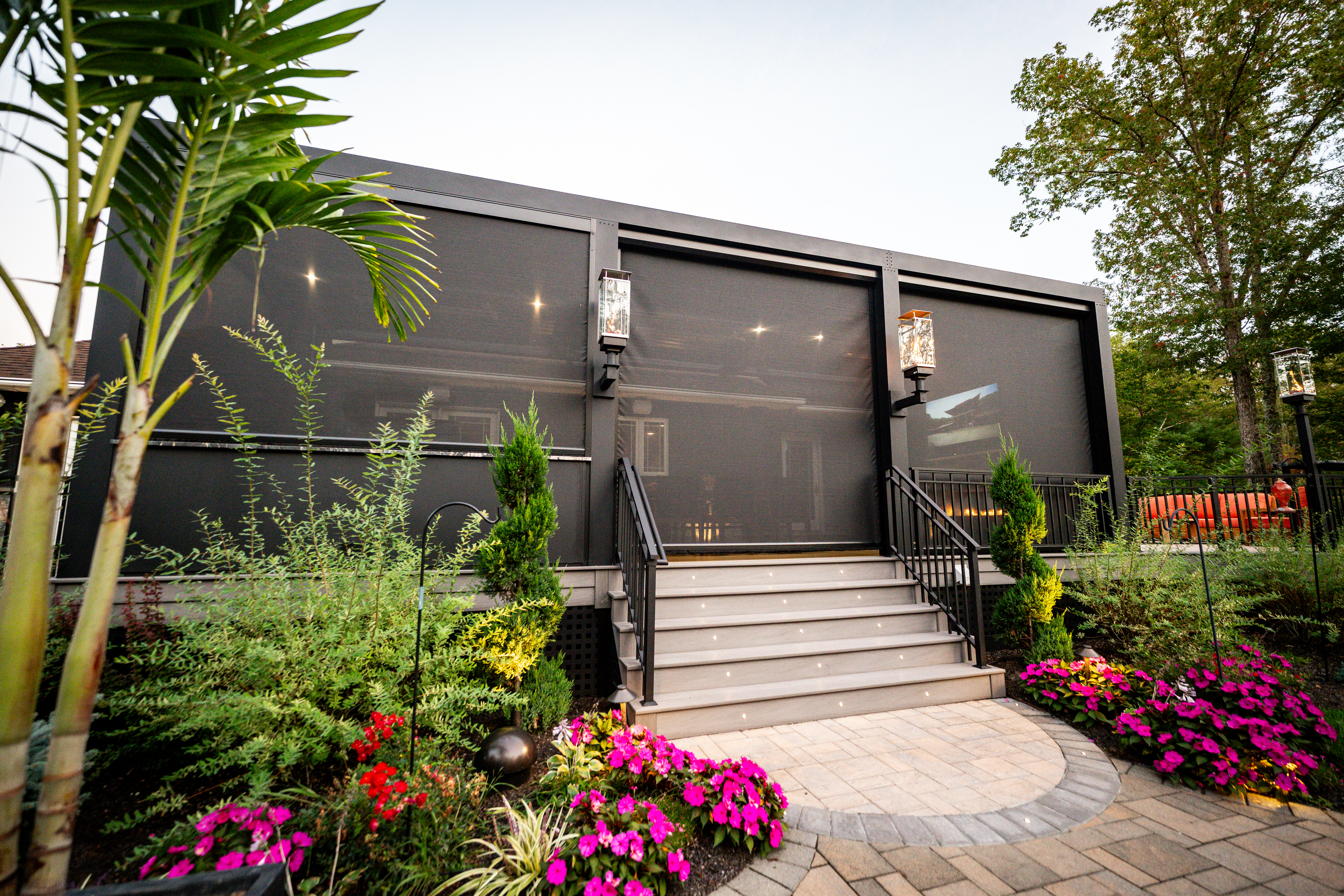 outdoor living space with motorized screens, centered stair entry, and landscaped garden with flowers and pathway lighting