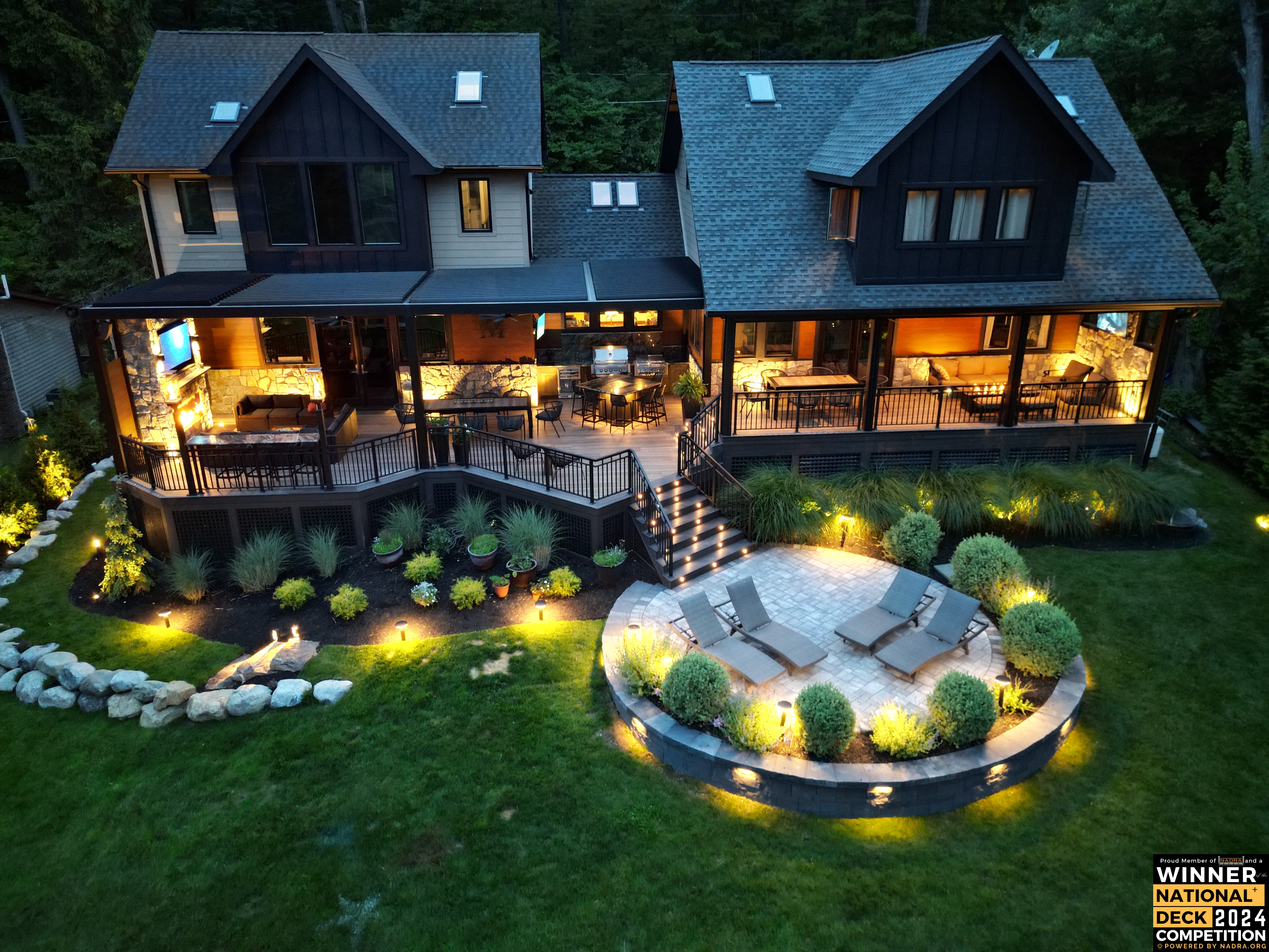 elevated multi-level deck with integrated stair lighting, louvered roof, under-rail lights, and landscape uplighting surrounding paver patio and curved retaining wall