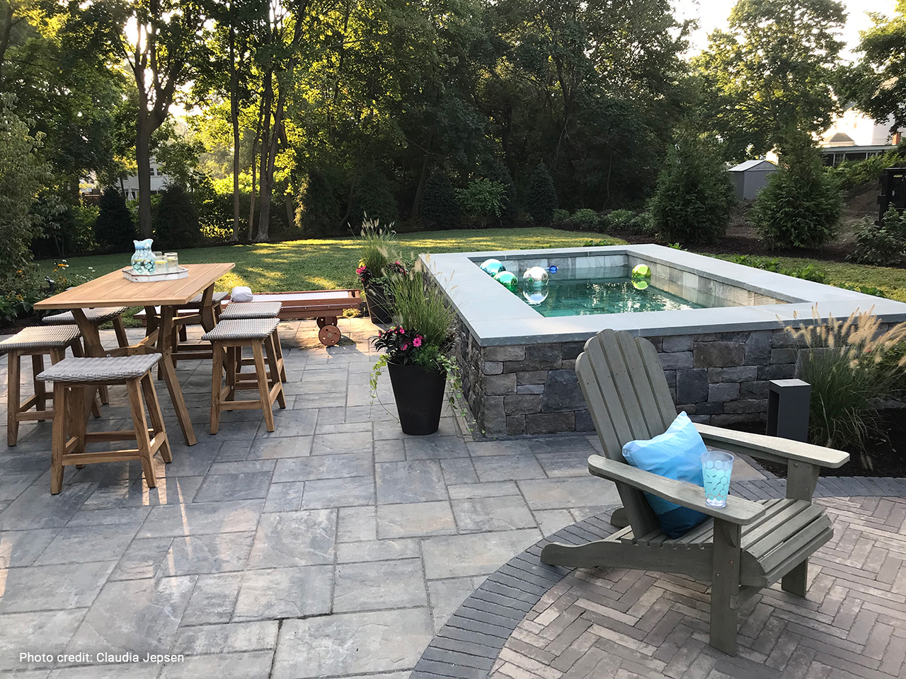 raised backyard plunge pool with stone surround integrated into paver patio, with dining area and seating nearby