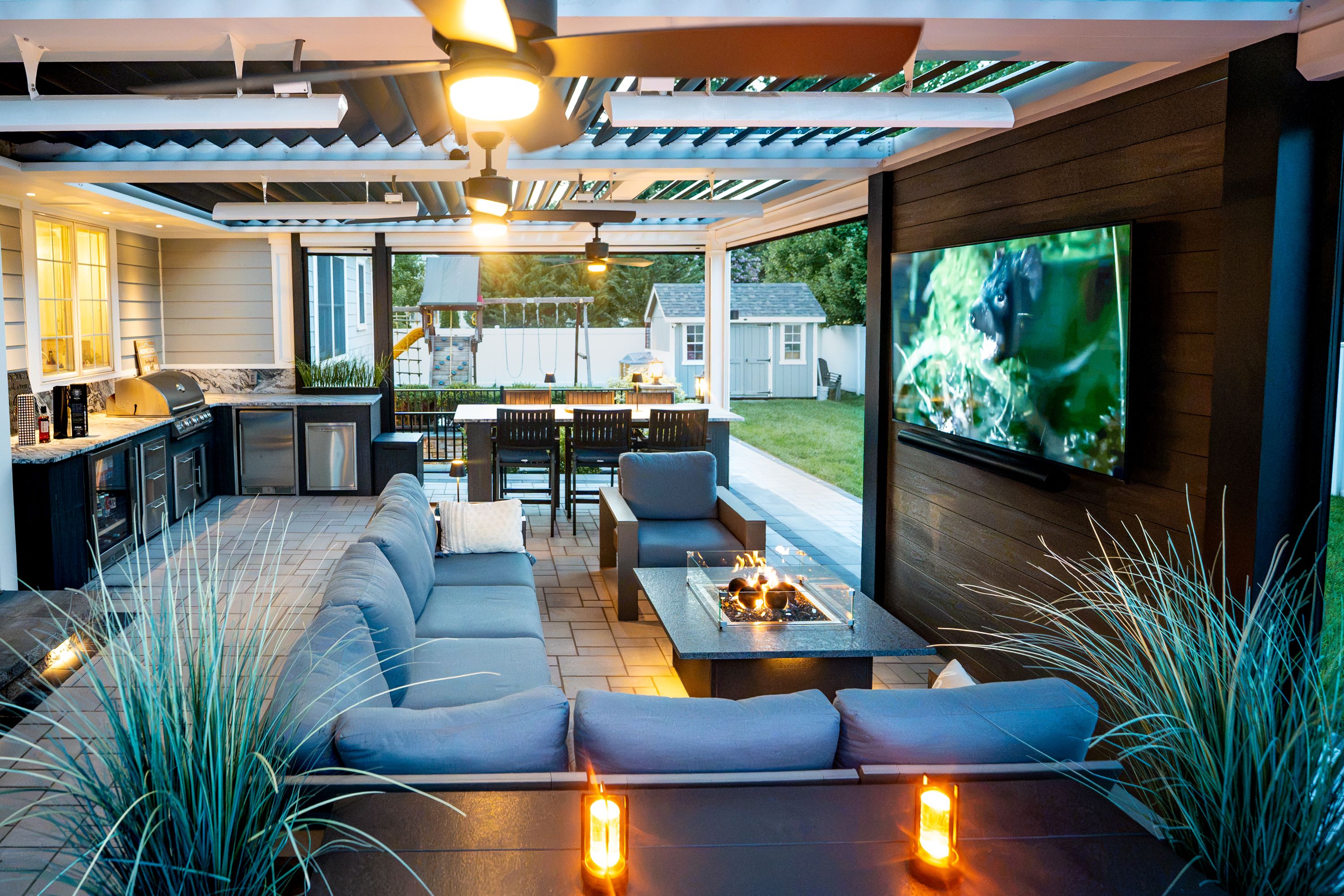louvered roof patio with sectional seating, fire table, outdoor TV, outdoor kitchen, and bar-height dining table