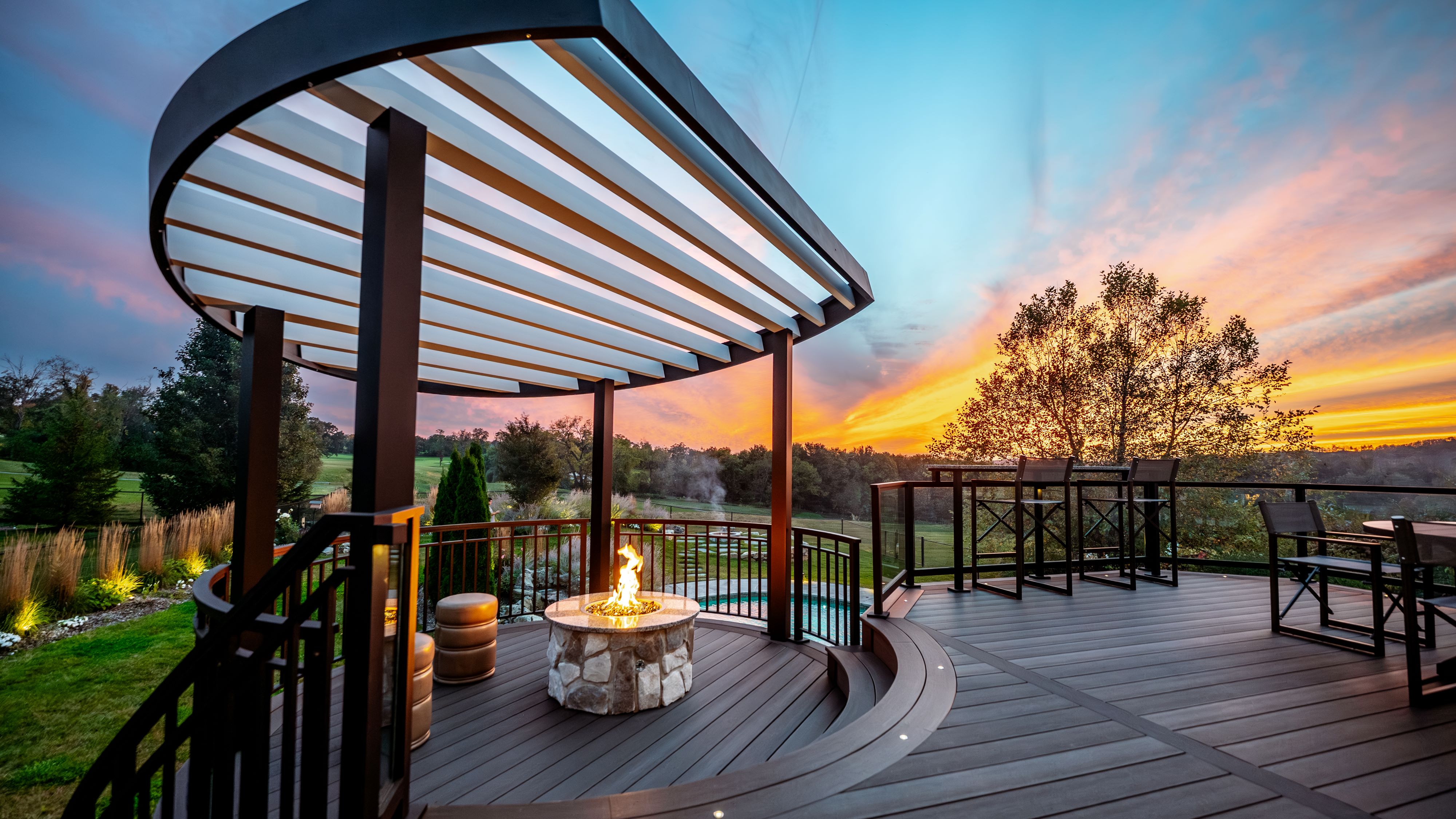 curved pergola shading a circular fire pit seating area on a multi-level deck overlooking a backyard landscape