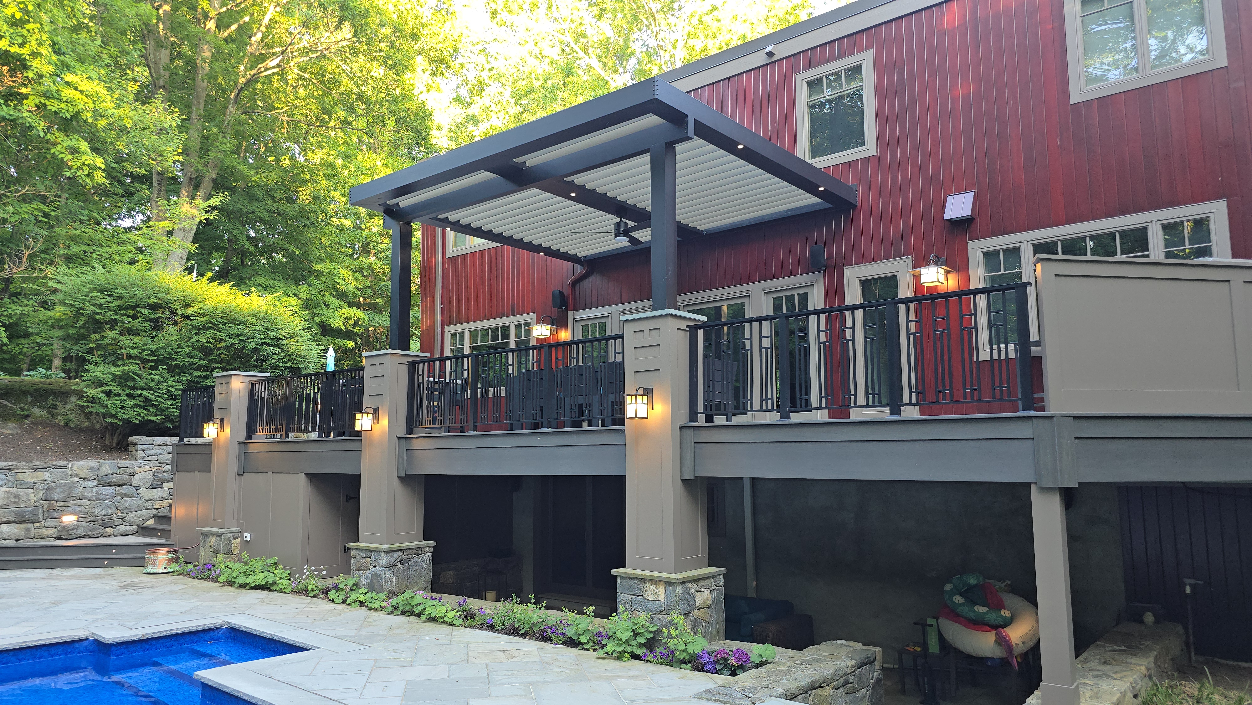 elevated backyard deck with louvered roof, railing and lighting, overlooking patio and small pool with landscaped surroundings