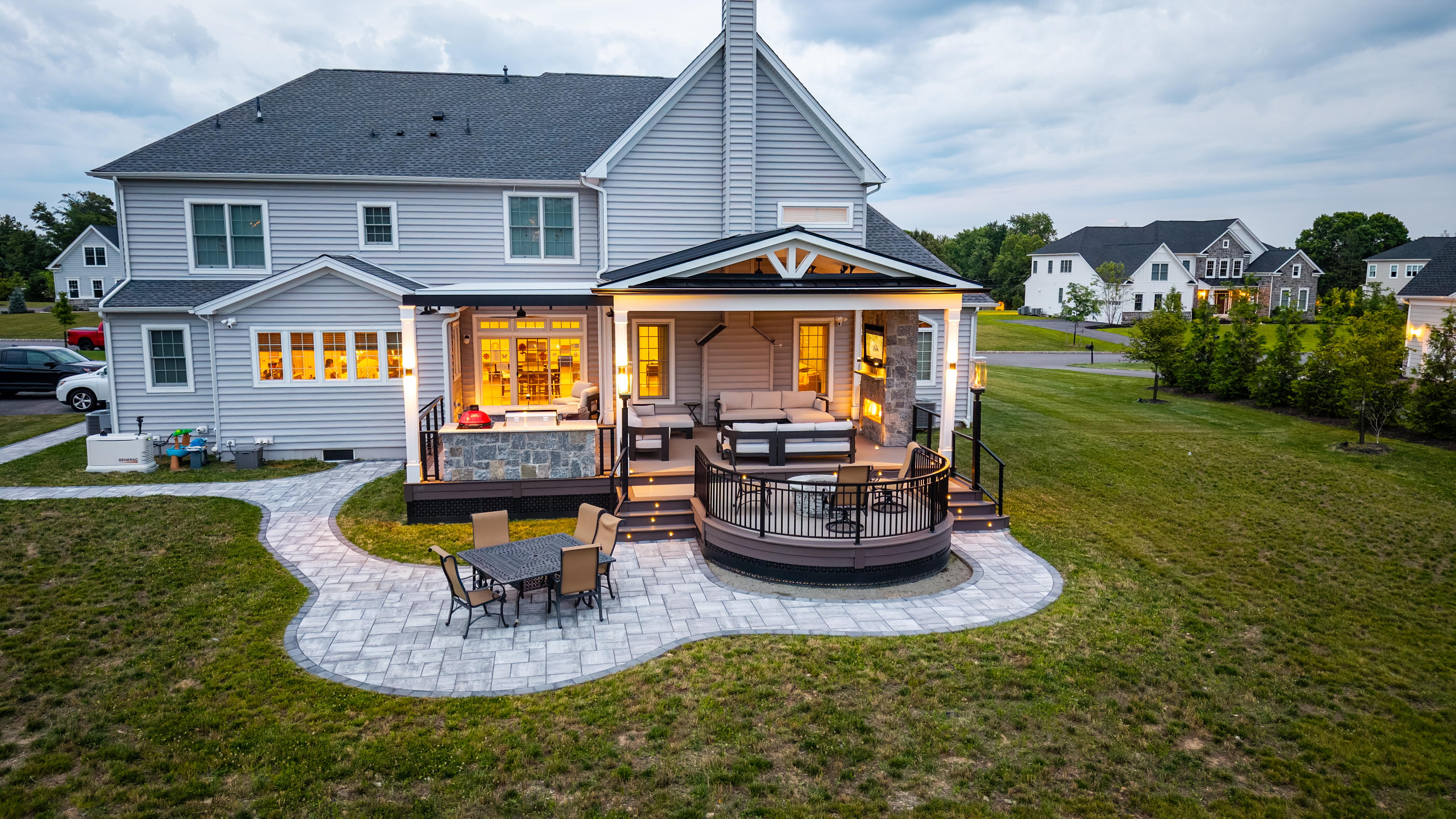 covered deck with traditional and louvered roofs, sectional seating and TV above a curved stone patio dining area
