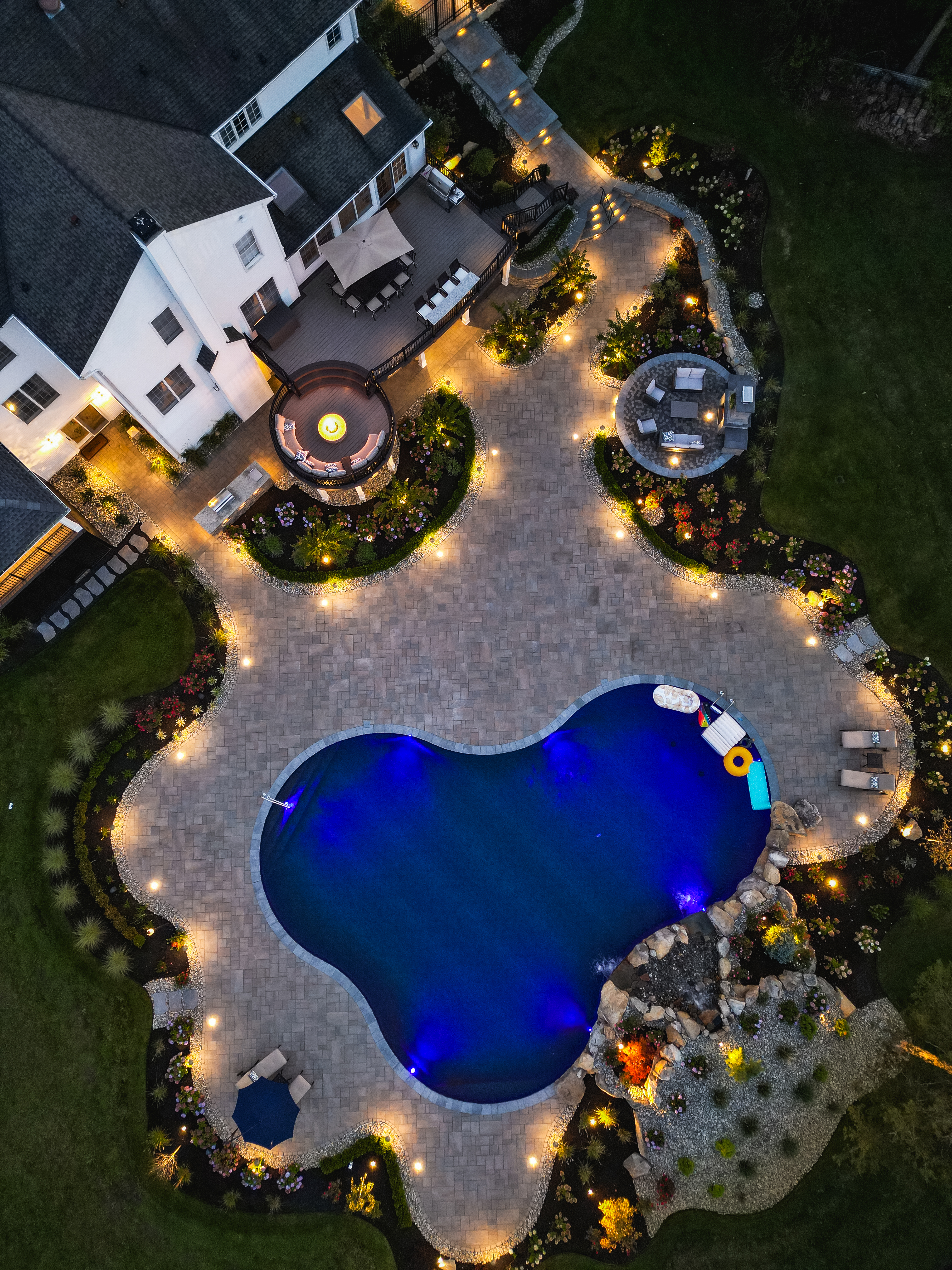 backyard pool and patio with landscape lighting accenting gardens, seating areas, and blue underwater pool lights
