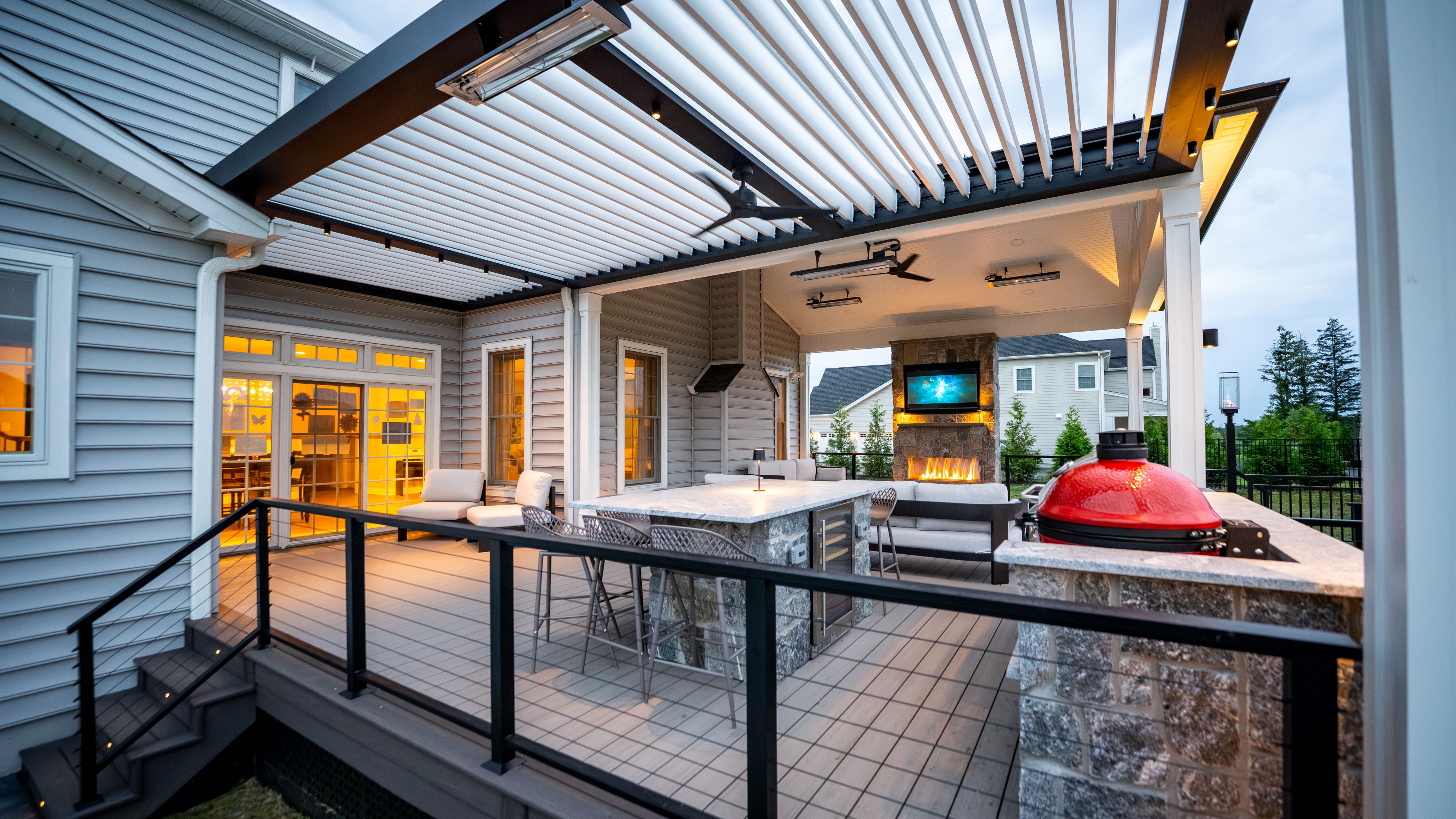 covered outdoor living space with louvered roof, outdoor kitchen, bar seating, couch, fireplace, and television