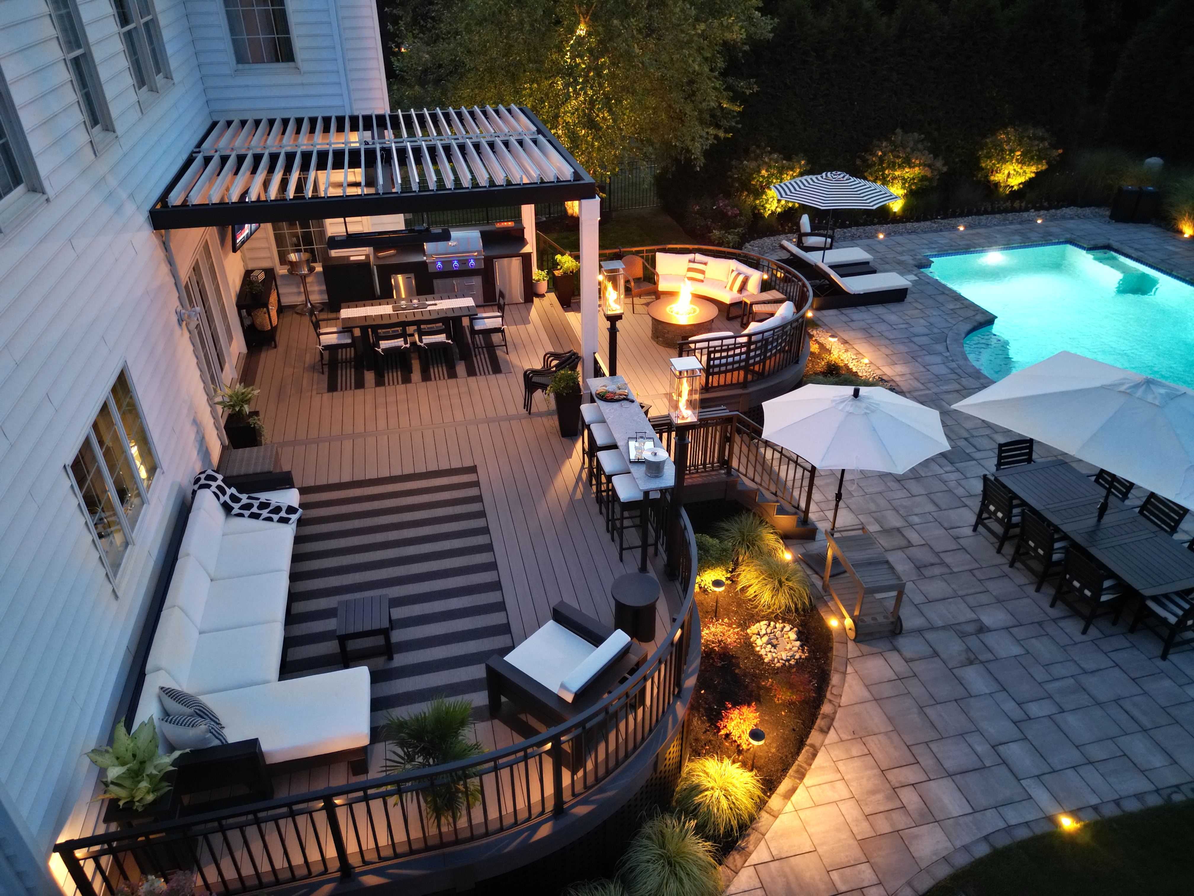 multi-level outdoor living space with deck lounge, covered kitchen area, fire pit seating, and poolside dining on paver patio