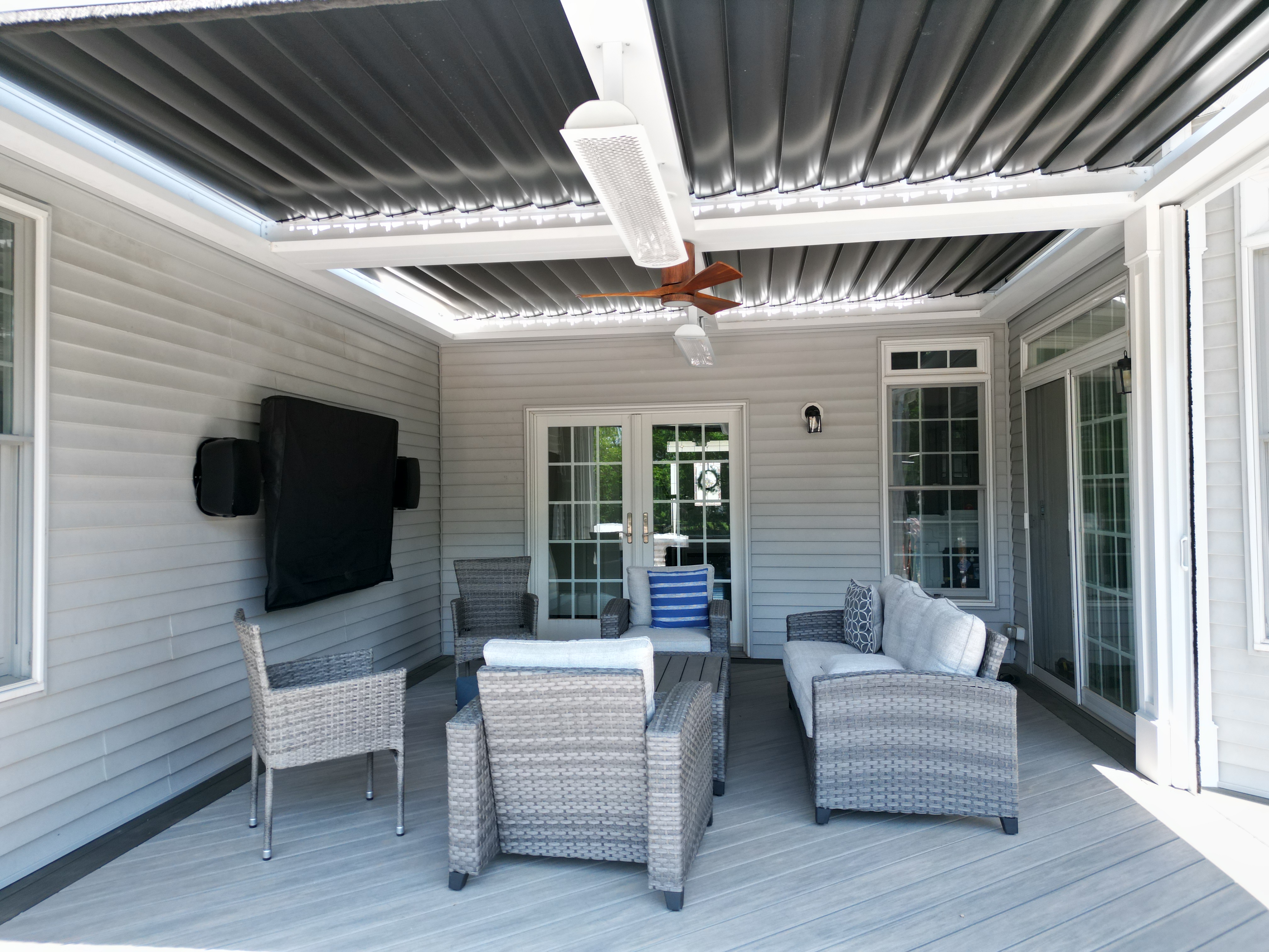 covered outdoor lounge area with wicker seating, ceiling fan, heaters, and adjustable louvered roof