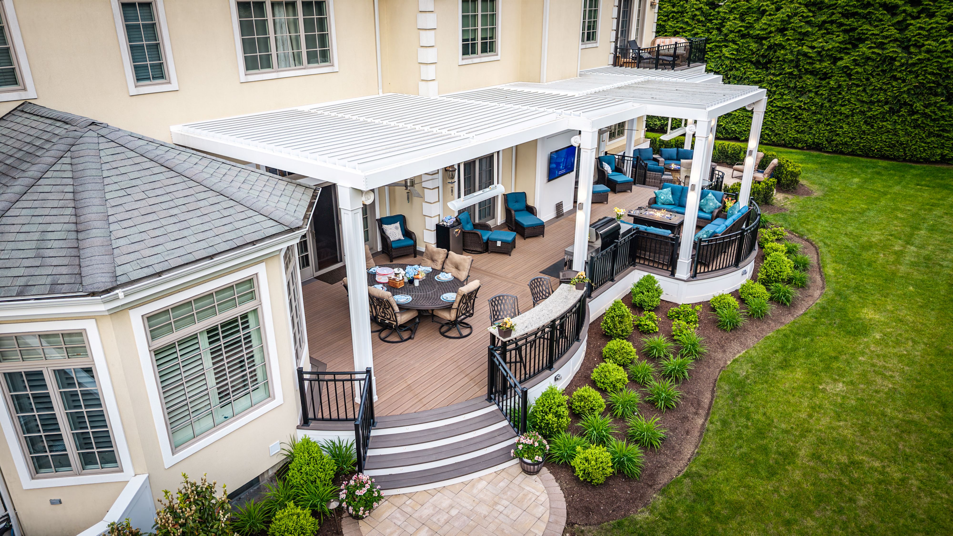 large outdoor deck with a motorized louvered roof covering outdoor dining, grilling, and lounge areas, overlooking patio seating area and landscape