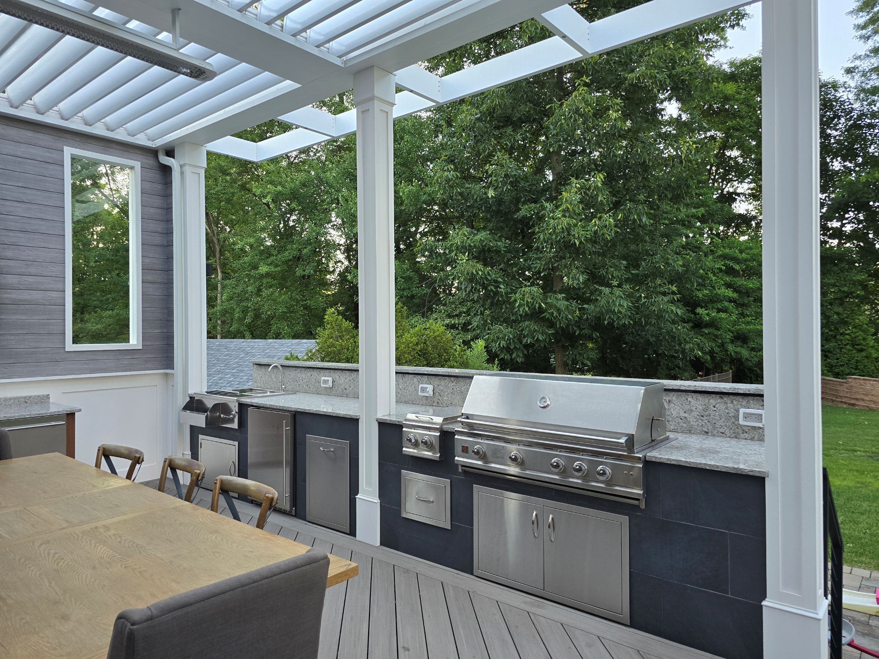 outdoor kitchen with stainless steel grill, side burner, sink, and granite countertops on a covered deck