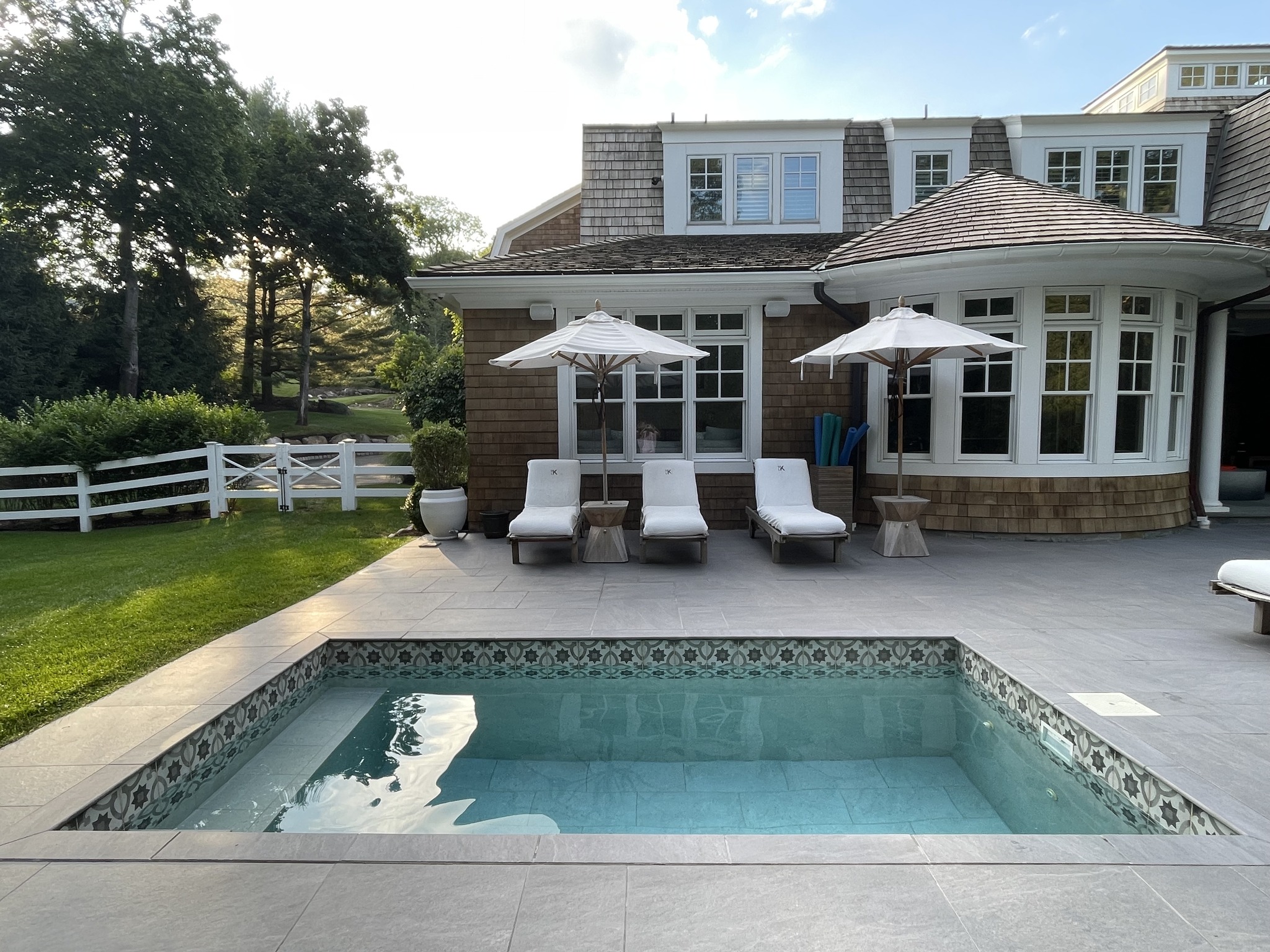 plunge pool set into patio with lounge chairs, umbrellas, and open backyard setting
